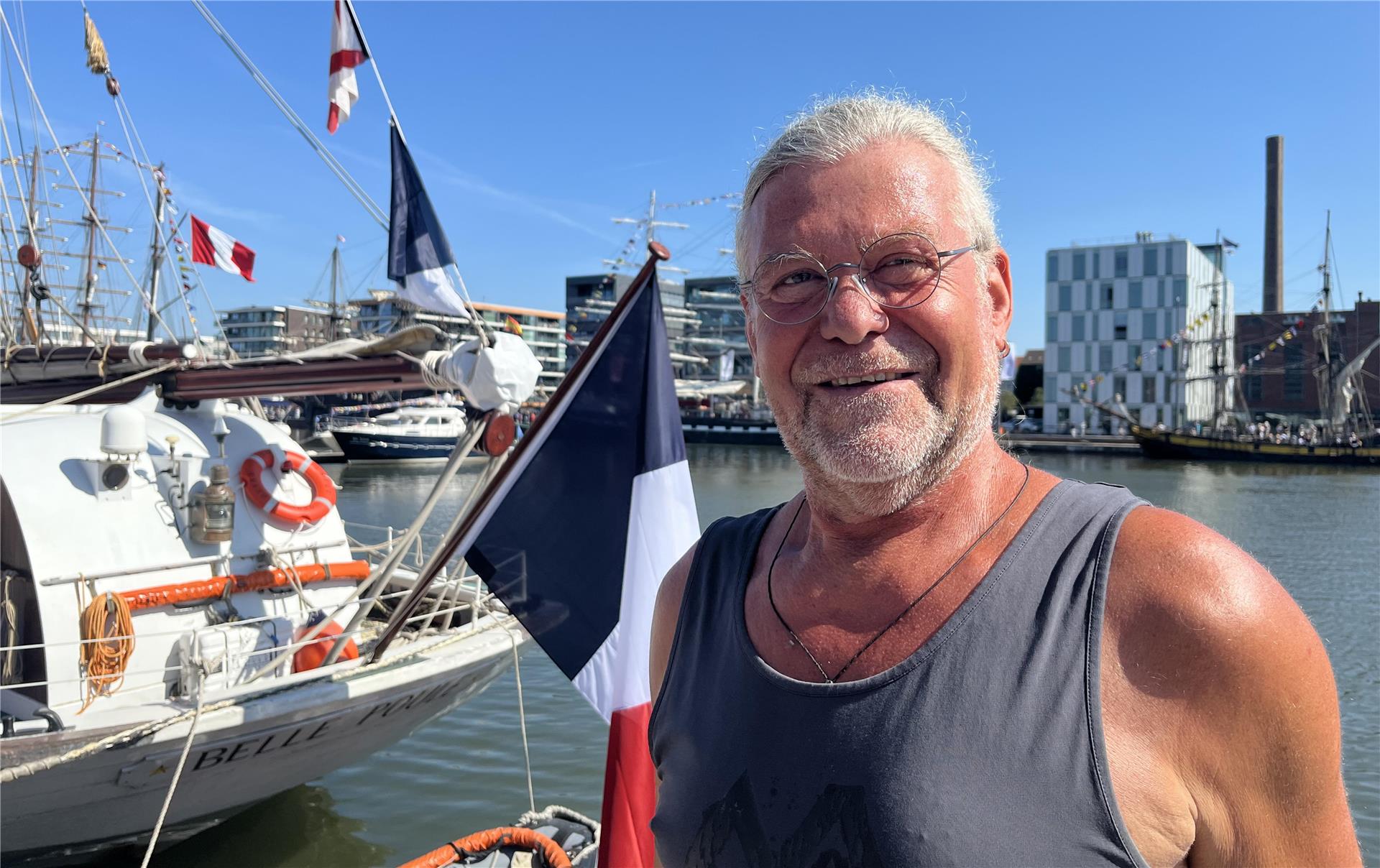 Ein Mann vor einem Schiff mit französischer Flagge.