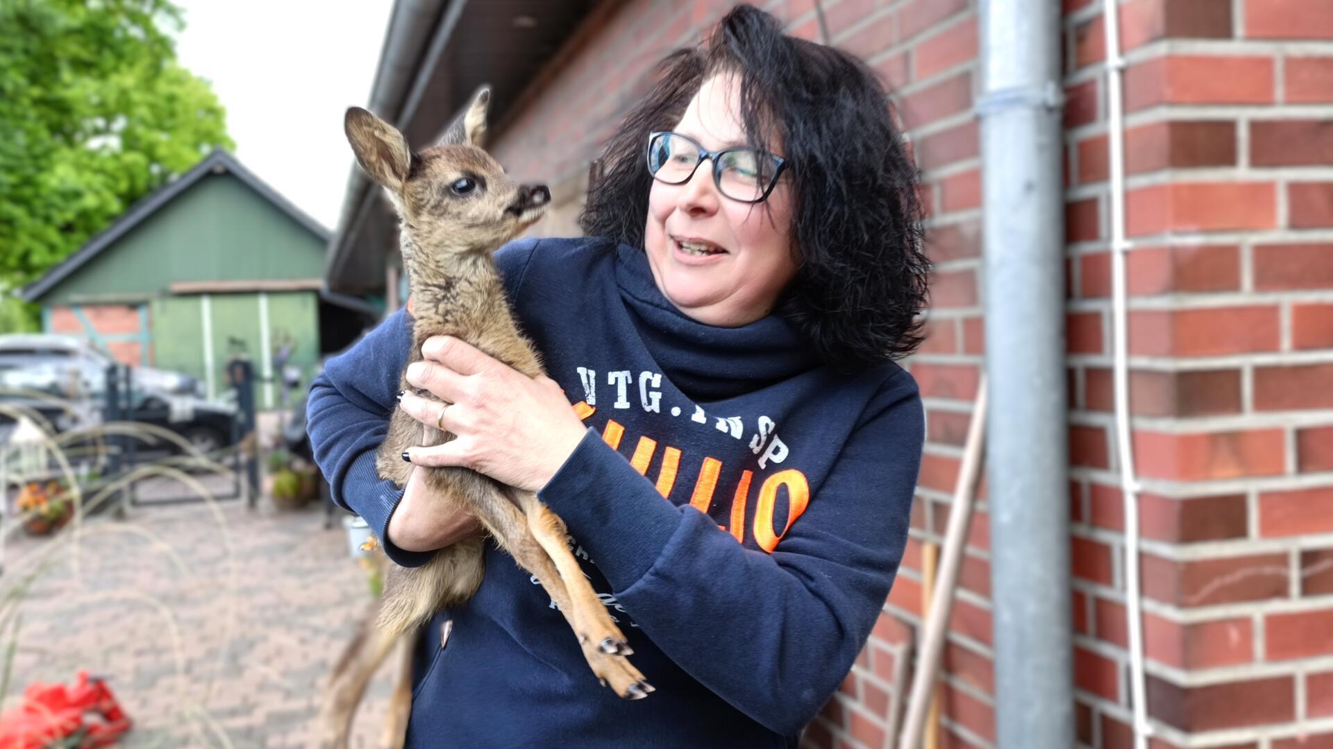 Eine Frau hält ein Reh-Kitz auf dem Arm. 