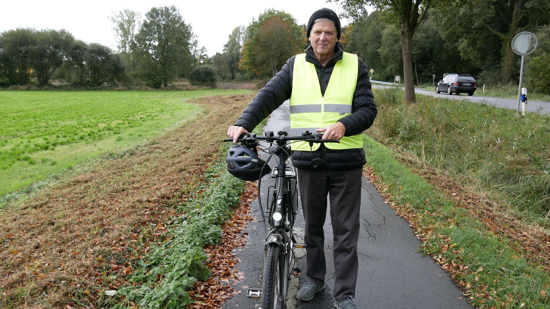 Ein Mann mit einer signalgelben Weste hält ein Fahrrad fest.