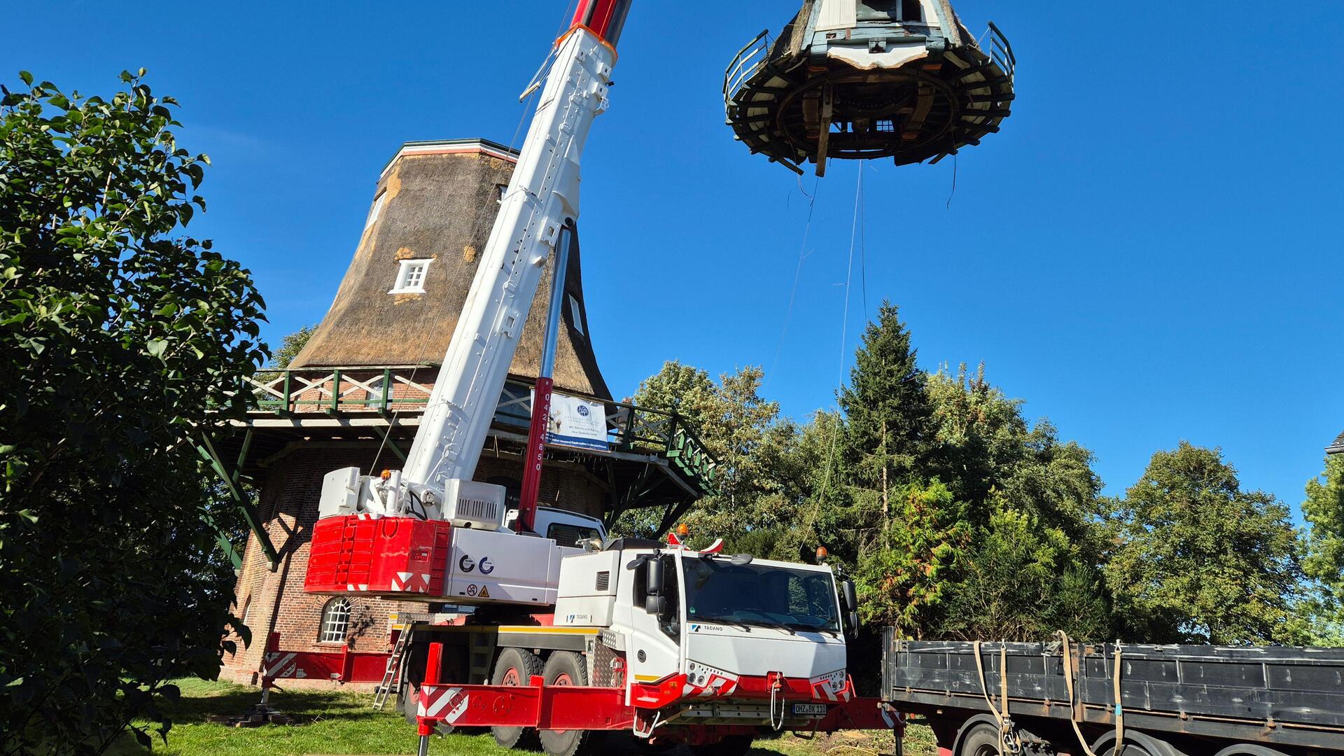 Ein Autokran hebt die Haube einer Galerieholländer-Windmühle ab