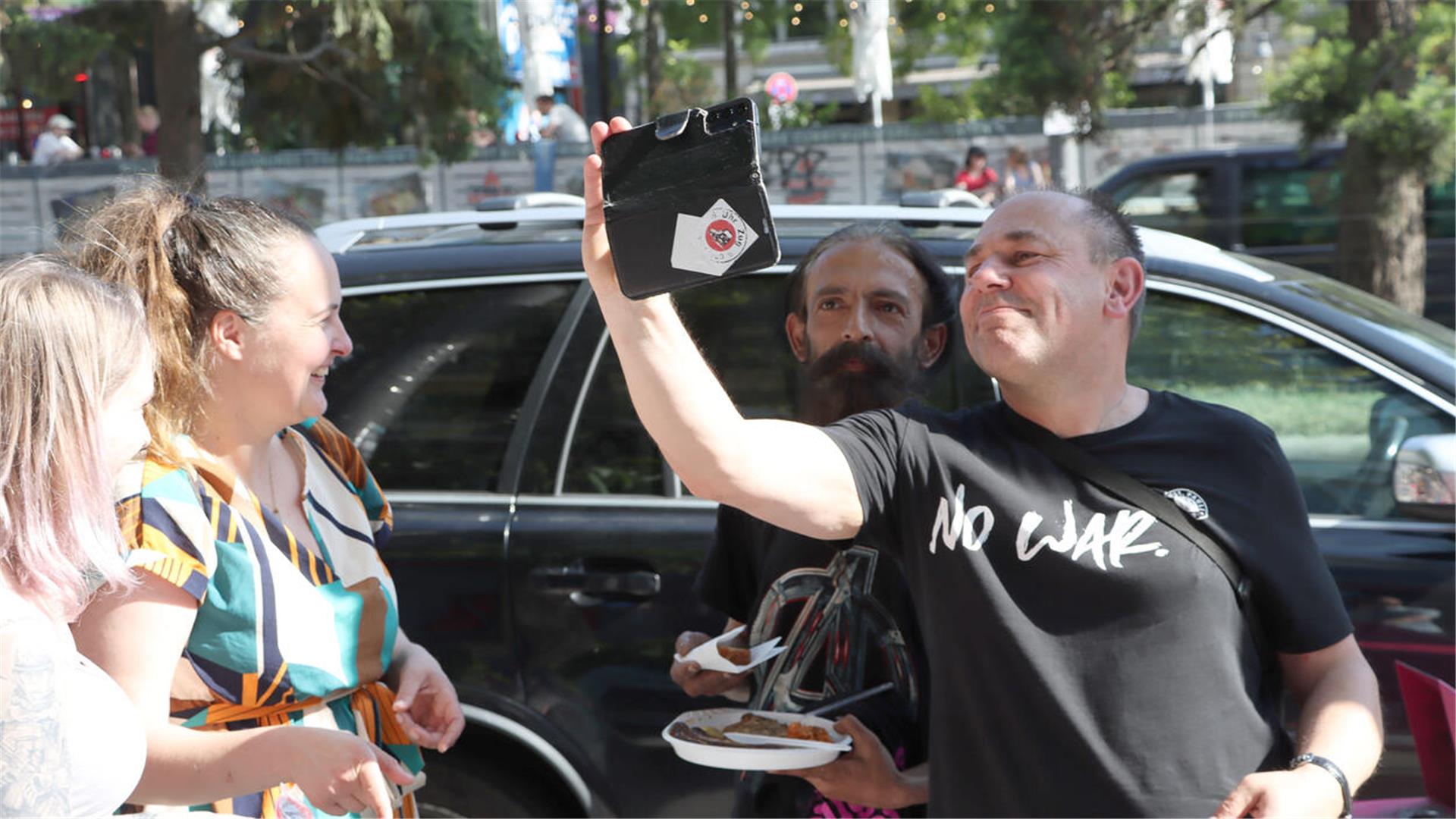 Ein Mann macht ein Selfie von sich und einem anderen Mann während zwei Frauen zuschauen.