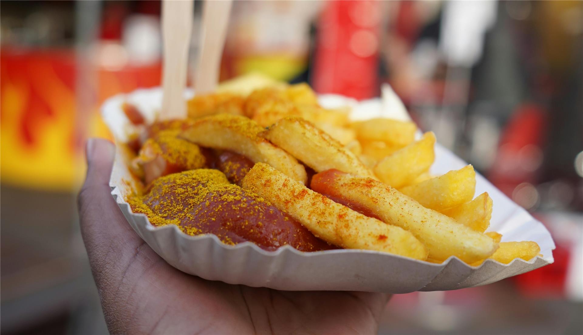 Eine Hand hält eine Papp-Schale mit Pommes und Currywurst.
