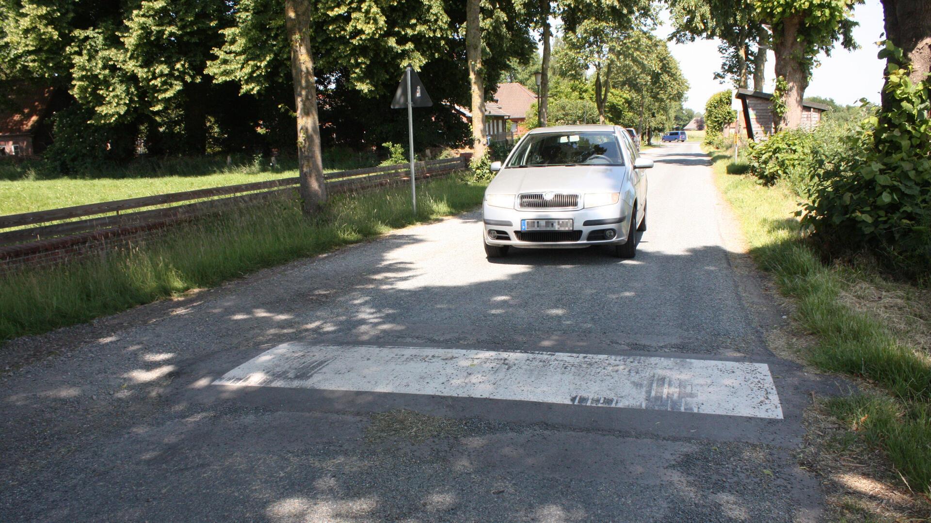 Ein silberner Pkw fährt auf einer schmalen Landstraße über eine neu installierte Fahrbahnschwelle in der Alten Lindenstraße in Dorfhagen.