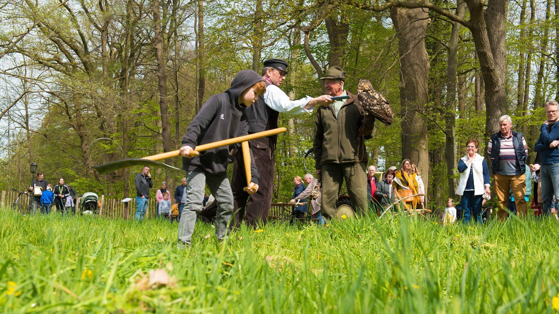 Mehrere Menschen demonstrieren, wie früher mit der Sense gemäht wurde