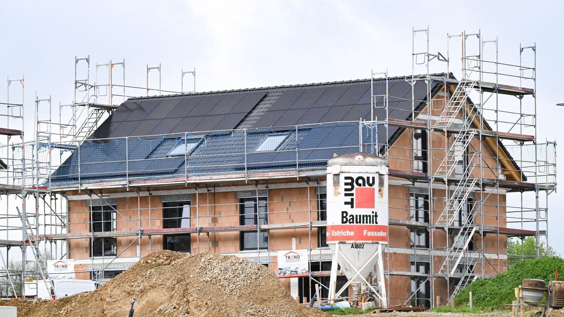 Ein unfertiges Mehrfamilienhaus. Das Dach ist gedeckt, Fenster sind eingesetzt. Ein Gerüst steht rund um den Neubau.