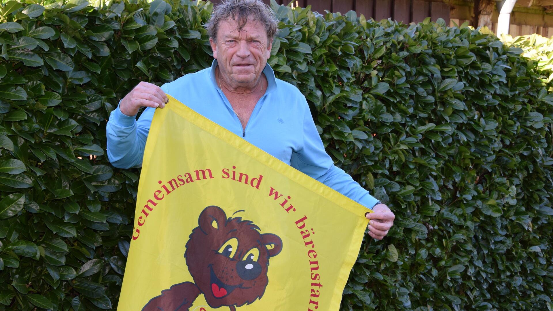  Der Vorsitzende des Selsinger Sozialverbandes, Theo Vonk, hält eine Fahne hoch auf der „Gemeinsam sind wir bärenstark“ steht.