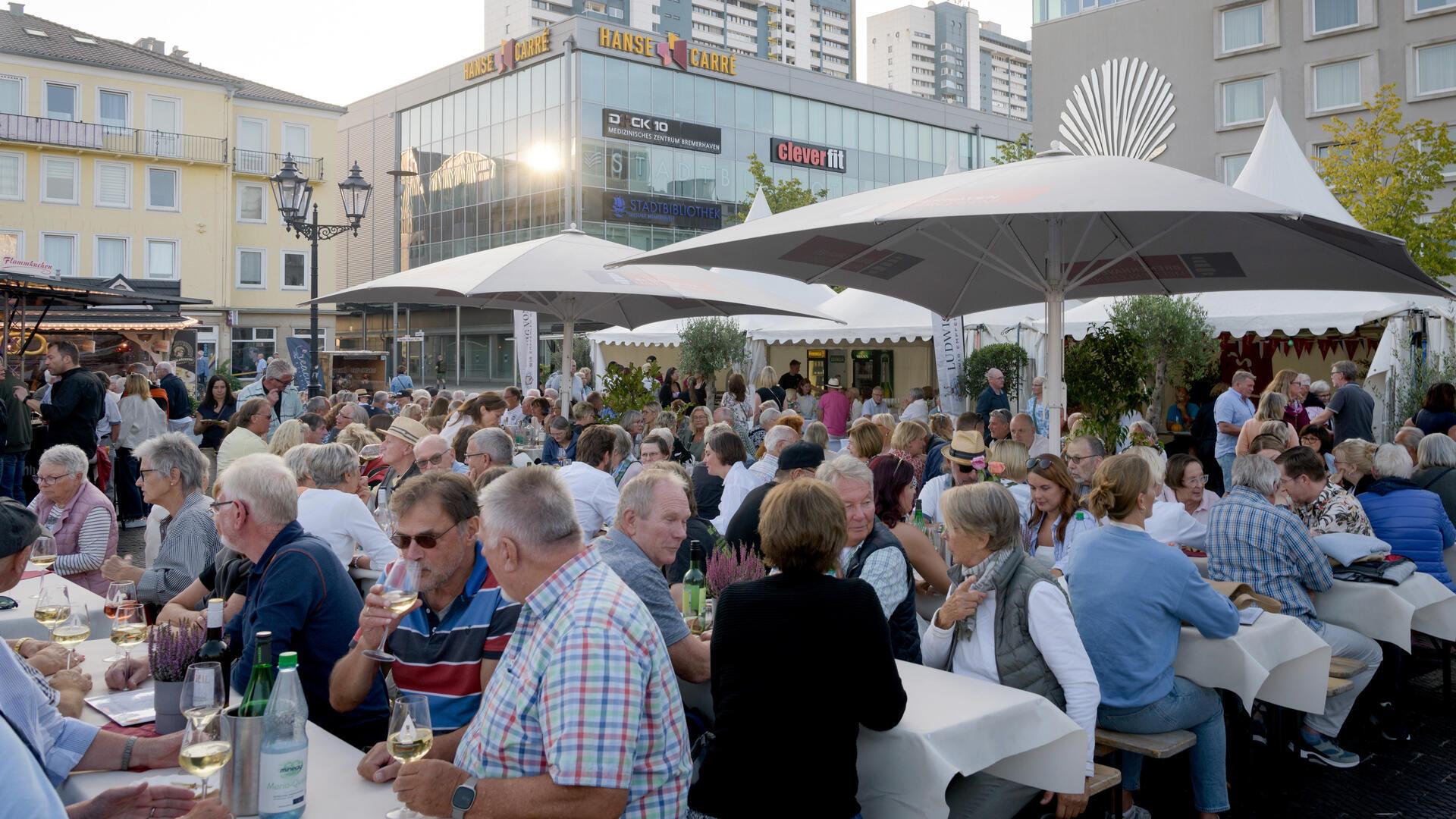 Viele Leute essen und trinken draußen an langen Tischen. 