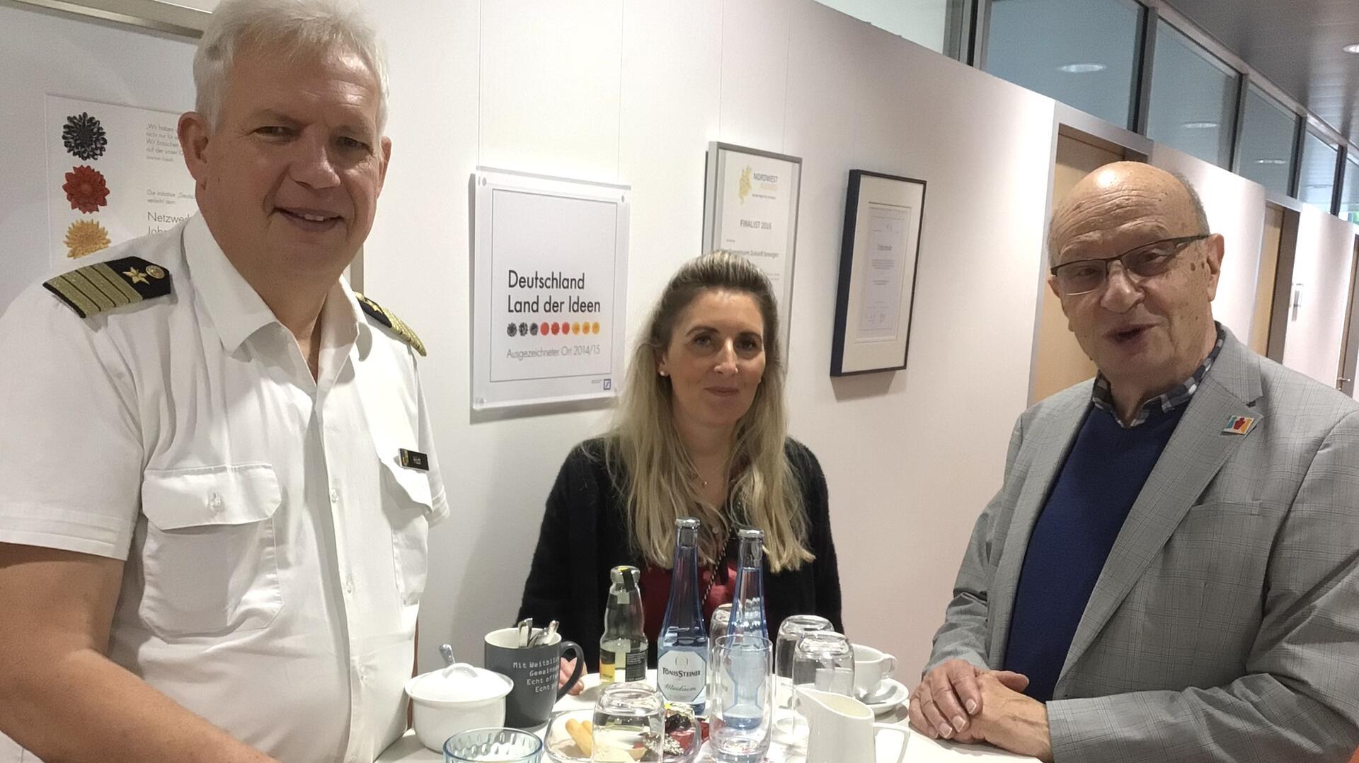 Drei Personen an einem Stehtisch blicken in die Kamera.