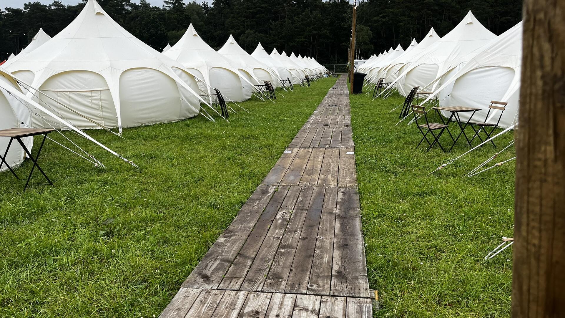 Zelt-Rivalen: Glamping-Luxus gegen Camping-Romantik beim Hurricane Festival Weiße Zelte mit einem Holzsteg in der Mitte.