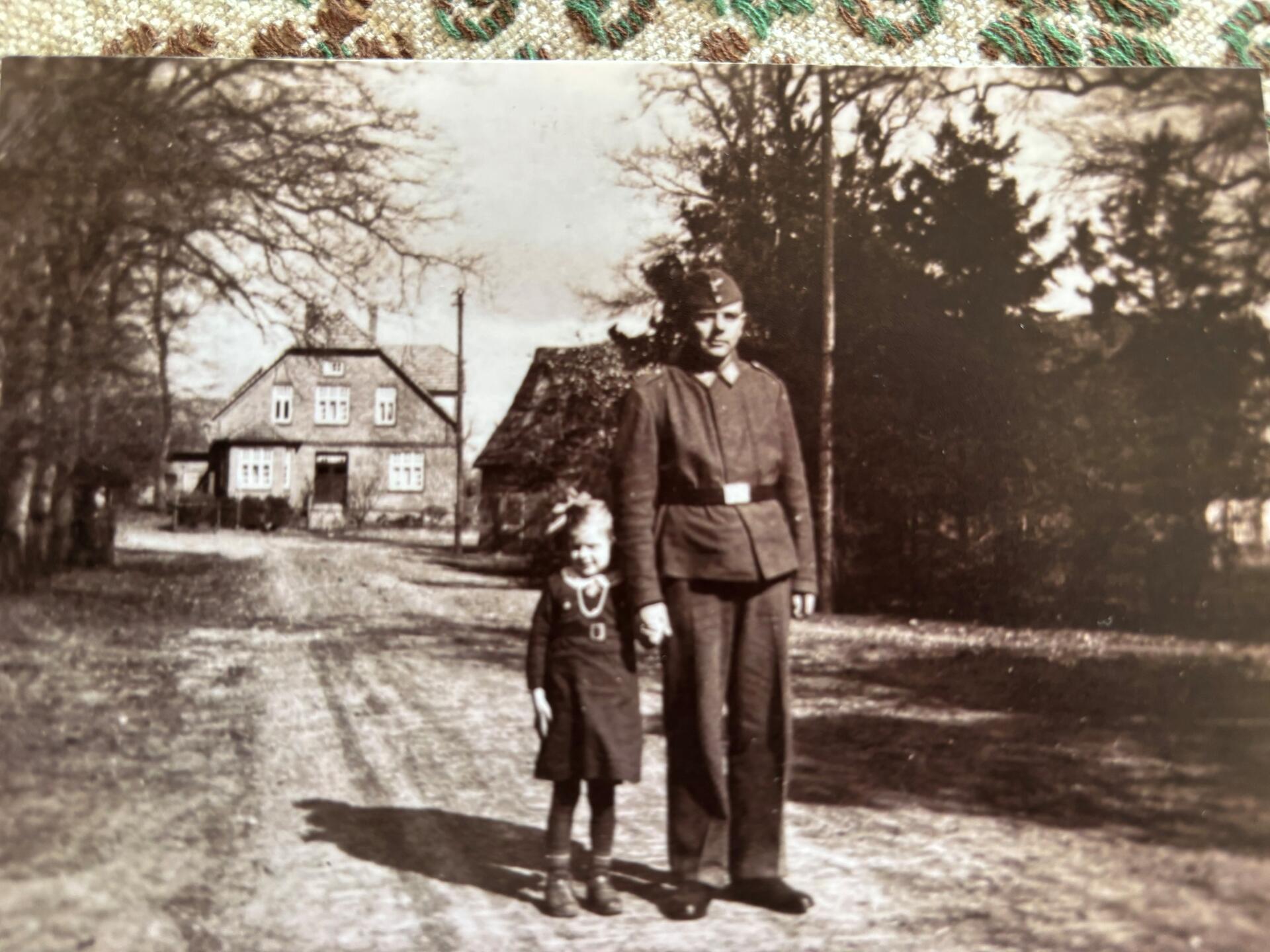 Ein Mann in Uniform und ein Mädchen stehen auf einer Straße und blicken in die Kamera.