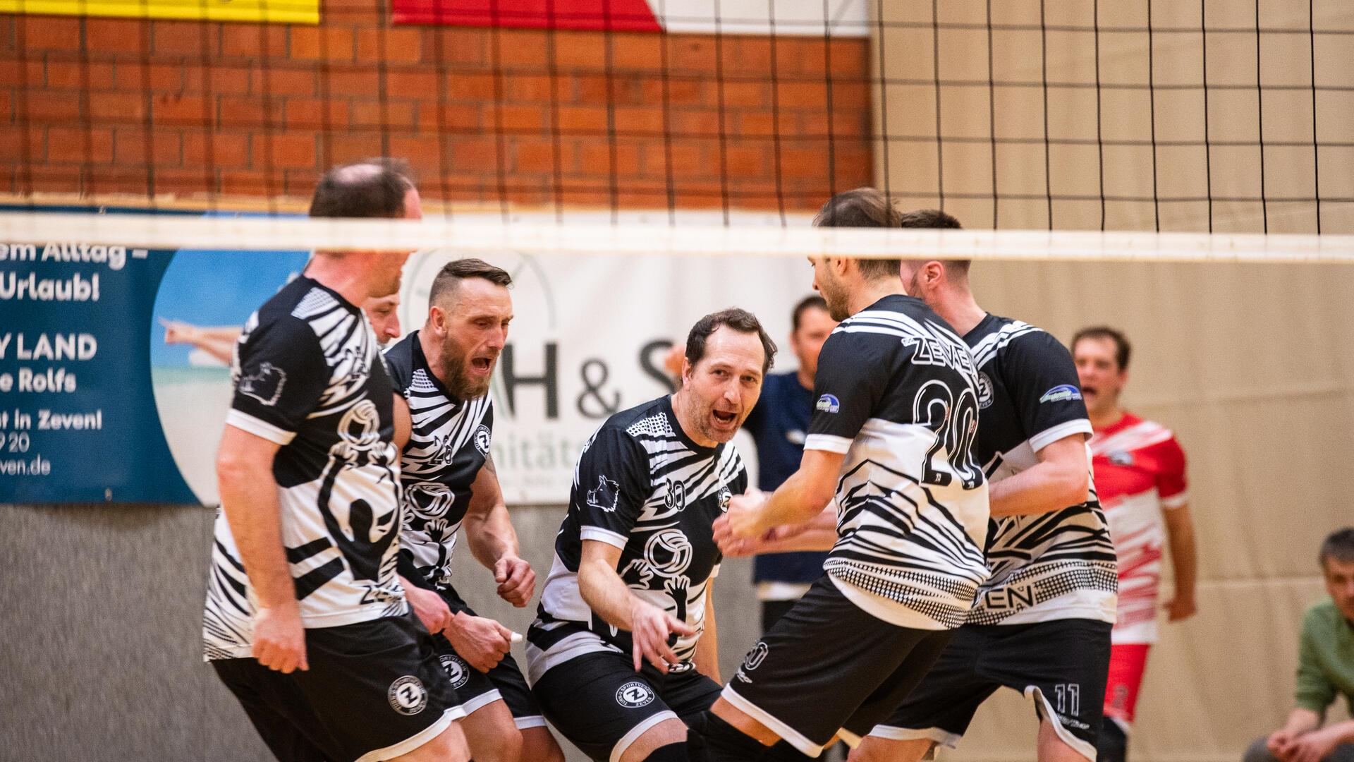 Männer hinter einem Volleyballnetz, die gemeinsam jubeln. 