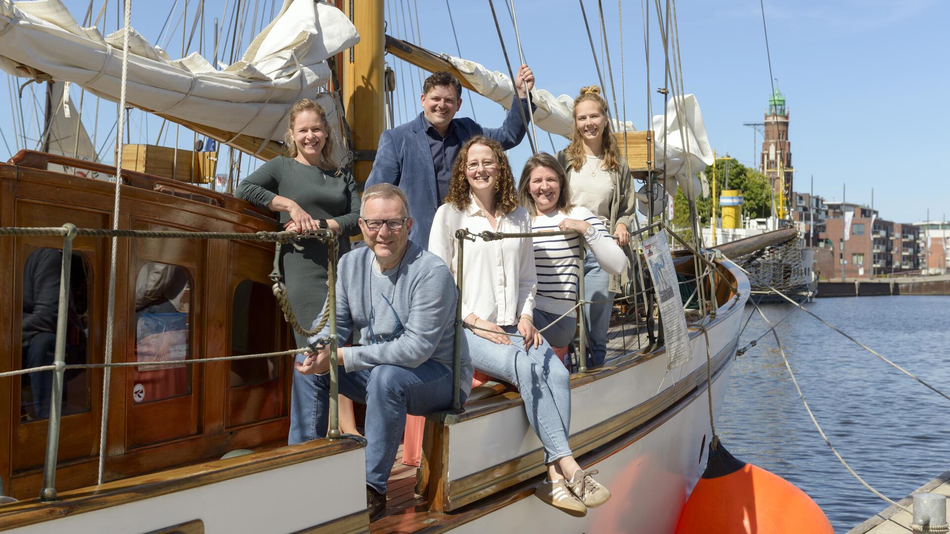 Mehrere Menschen stehen lächelnd auf einem Boot im Becken des Neuen Hafens. 