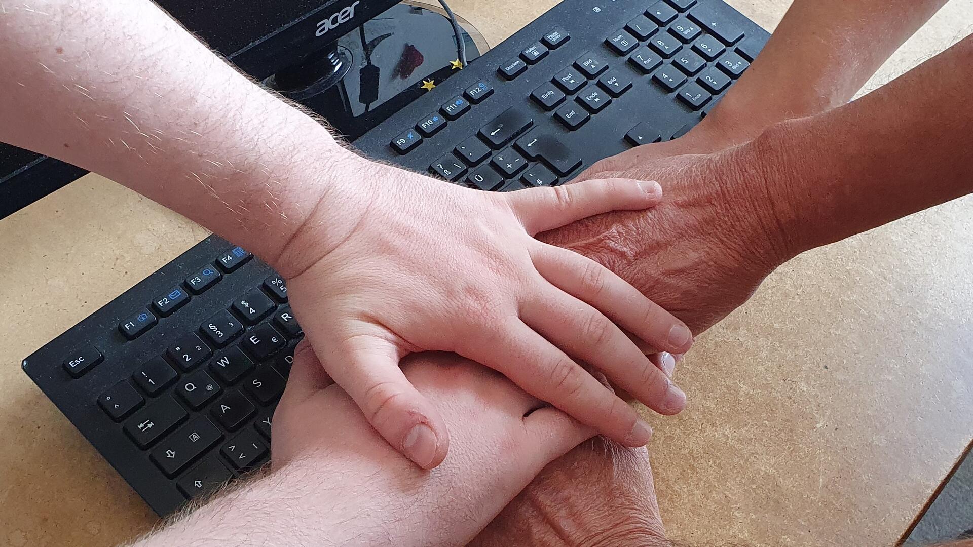 Fünf Hände übereinander auf einer Tastatur