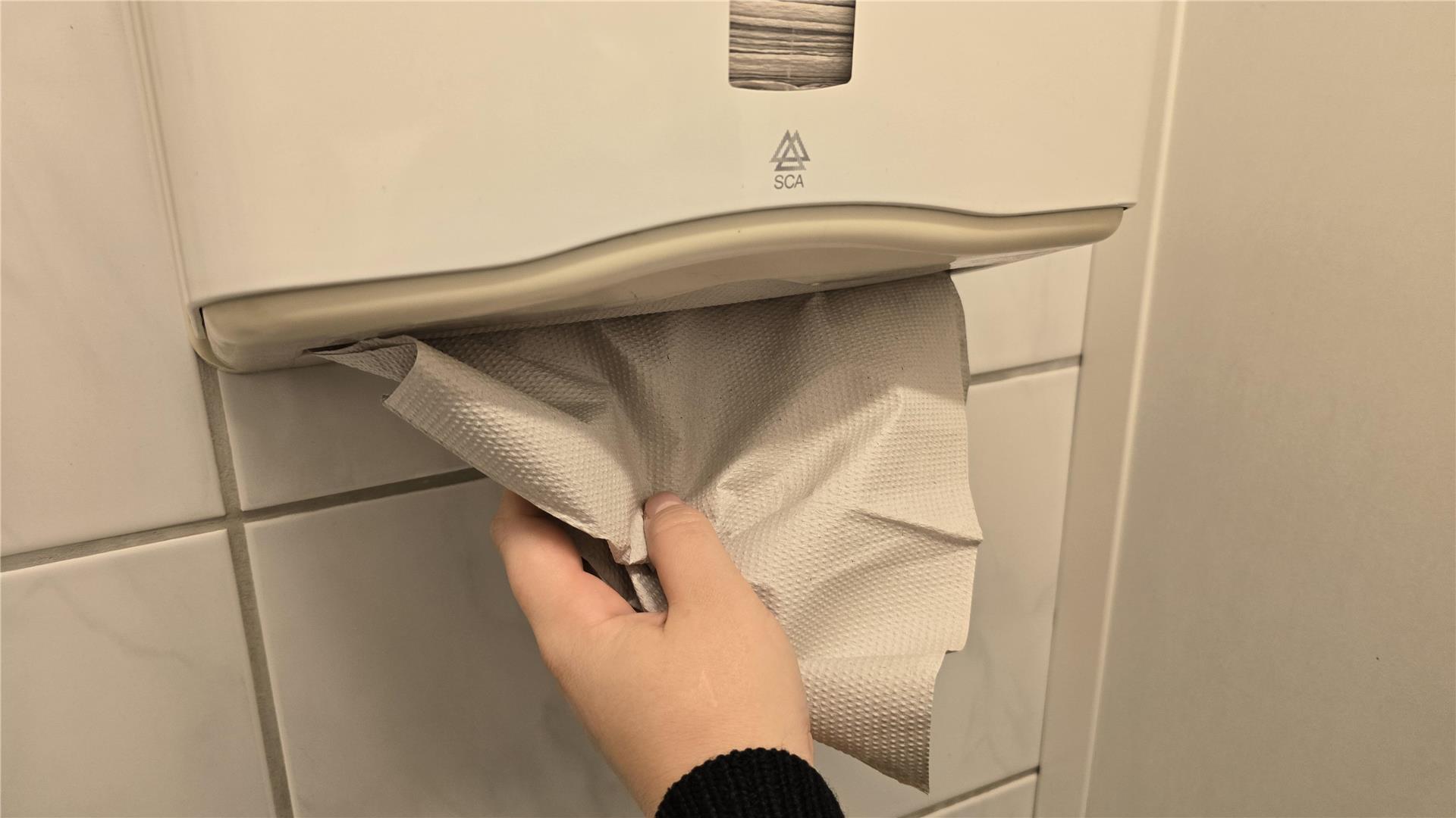 Eine Hand greift nach Papierhandtüchern in einem Spender