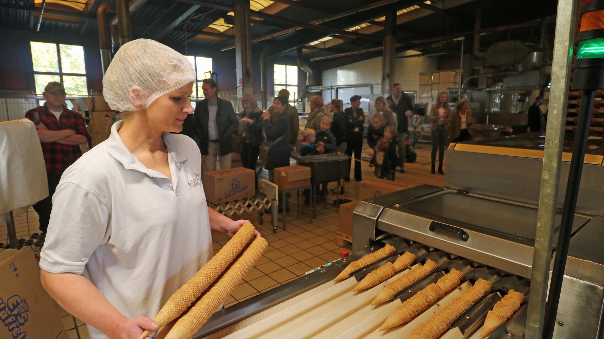 Viele Menschen in einer Halle. Im Vordergrund eine Frau. In den Händen hält sie frisch produzierte Eiswaffeln