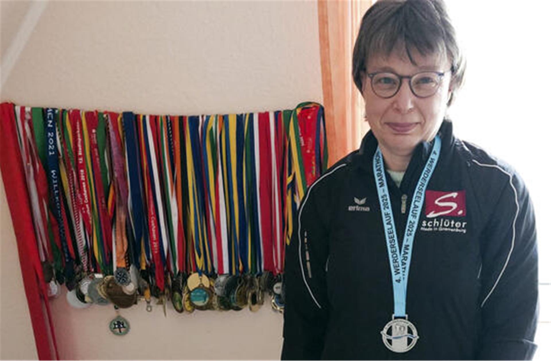 Heike Lubes mit der Medaille für die erfolgreiche Teilnahme am „Werderseelauf“ um den Hals und mit 49 weiteren Medaillen von Marathonläufen neben ihr an der Wand.