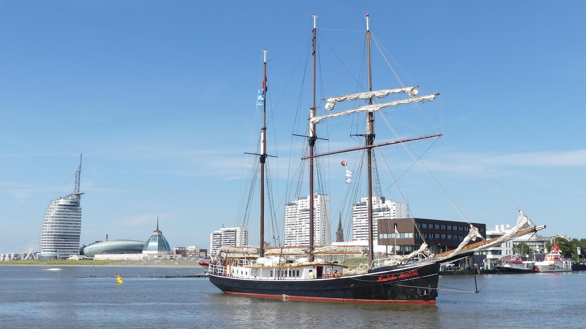 Ein Schiff fährt auf dem Wasser. Im Hintergrund ist die Silhouette einer Stadt zu sehen.