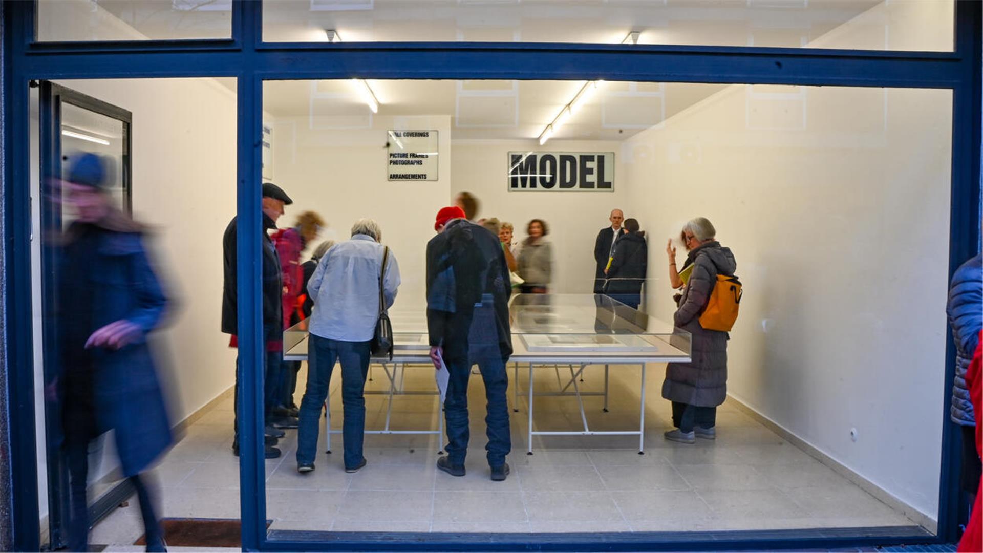 Hinter einem Schaufensterfenster stehen Menschen und gucken in Ausstelliungsvitrinen. 