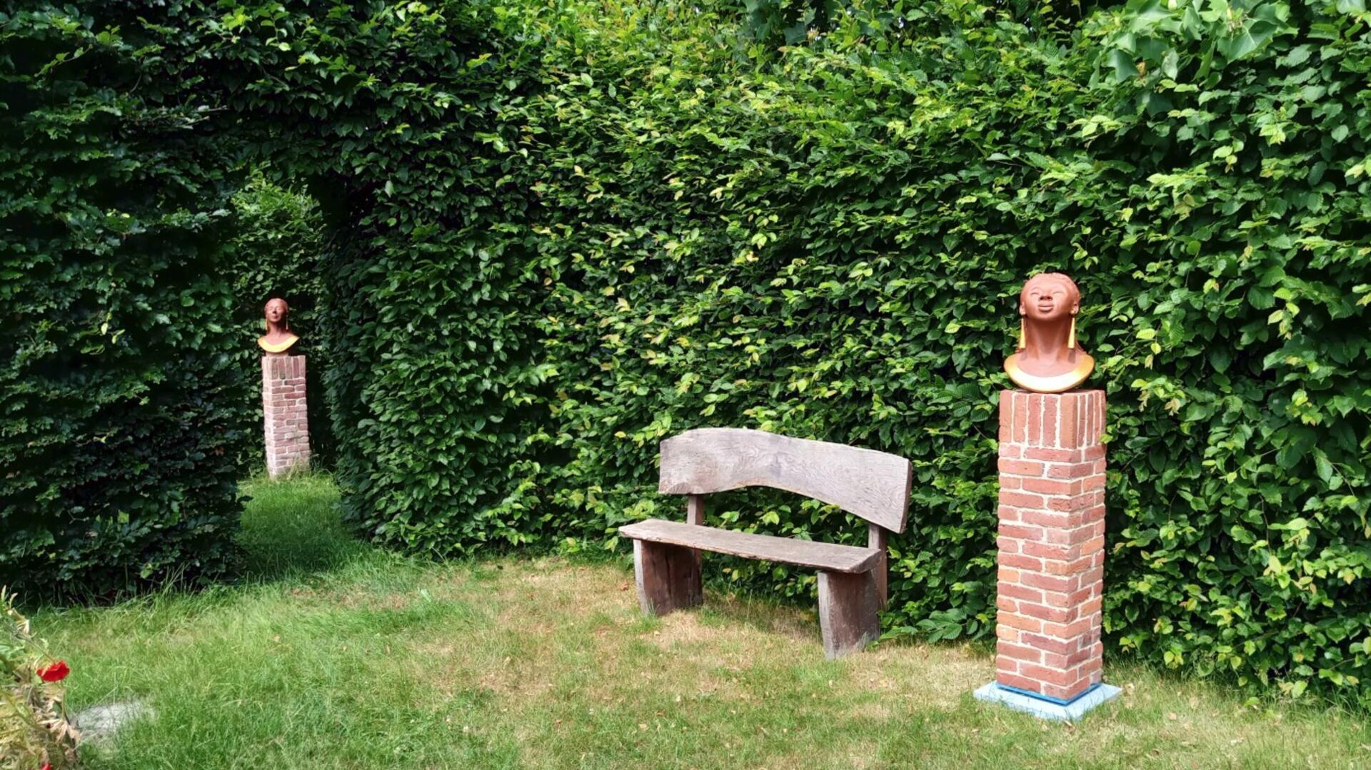 Ein Garten, in dem unter anderem eine Bank vor einer Hecke steht. Und zwei Skulpturen sind zu sehen. Hinter hohen Hecken verborgen lädt der Garten der Epikurike in Nartum mit Skulpturen, seltenem Baumbestand und stillen Ecken zum Verweilen und Entdecken ein.