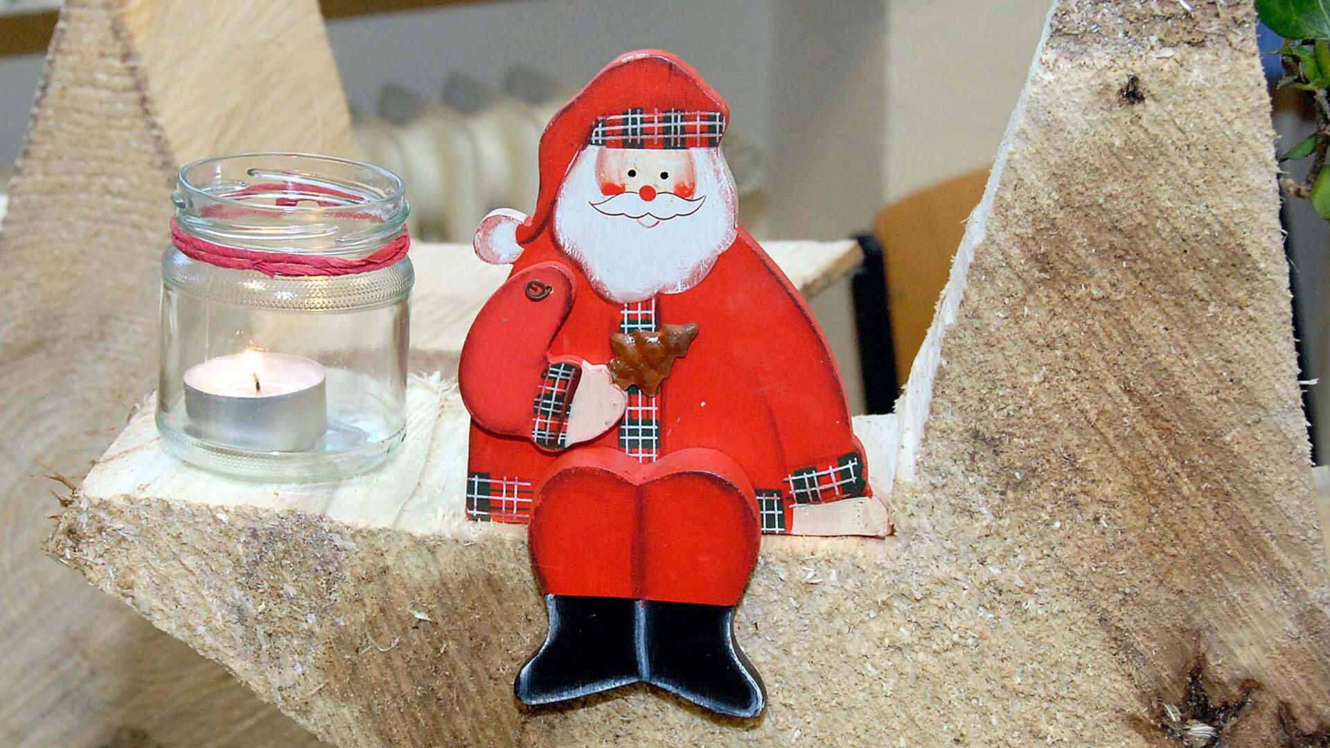 Kreativität trifft Gemütlichkeit: Basar im Seniorencentrum Ein Weihnachtsmann aus Holz sitzt neben einem Glas mit einer Kerze.