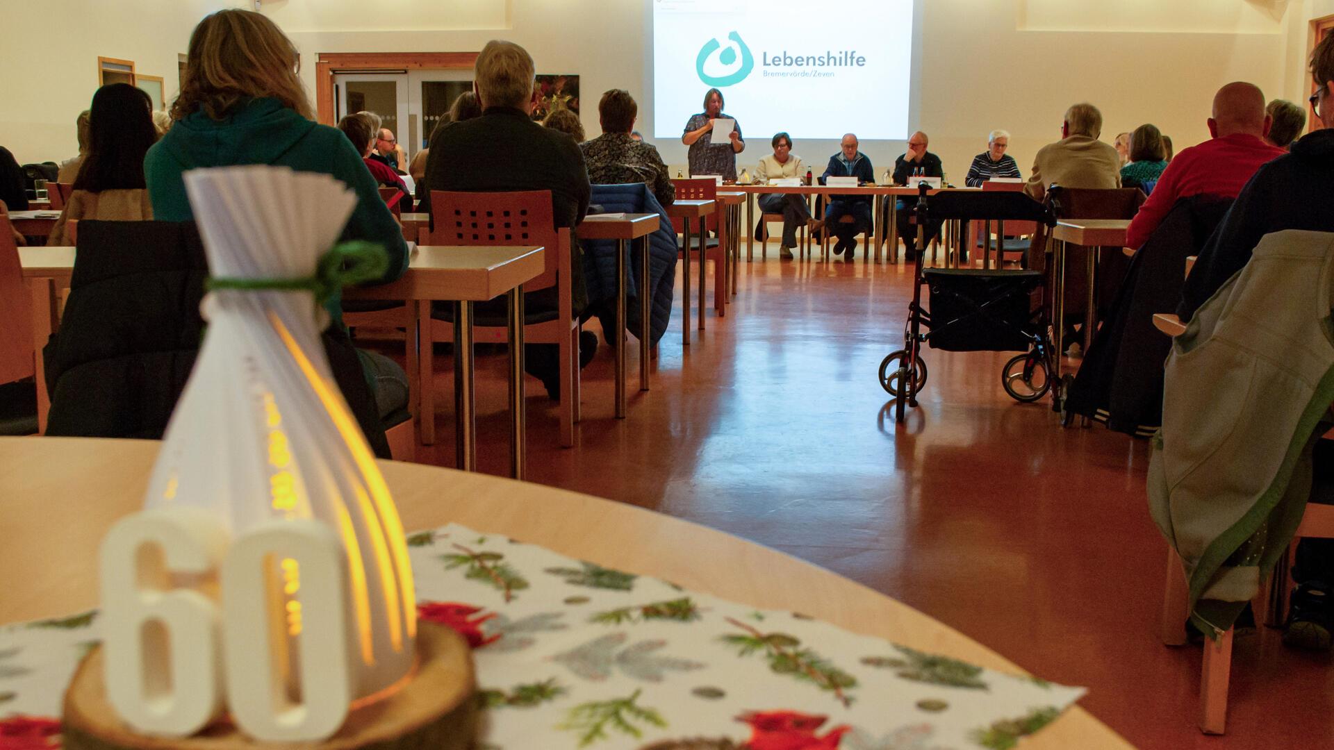 Menschen sitzen auf Stühlen und hören einer Gruppe Menschen zu, die sich vor ihnen ebenfalls auf Stühlen sitzend befindet. 