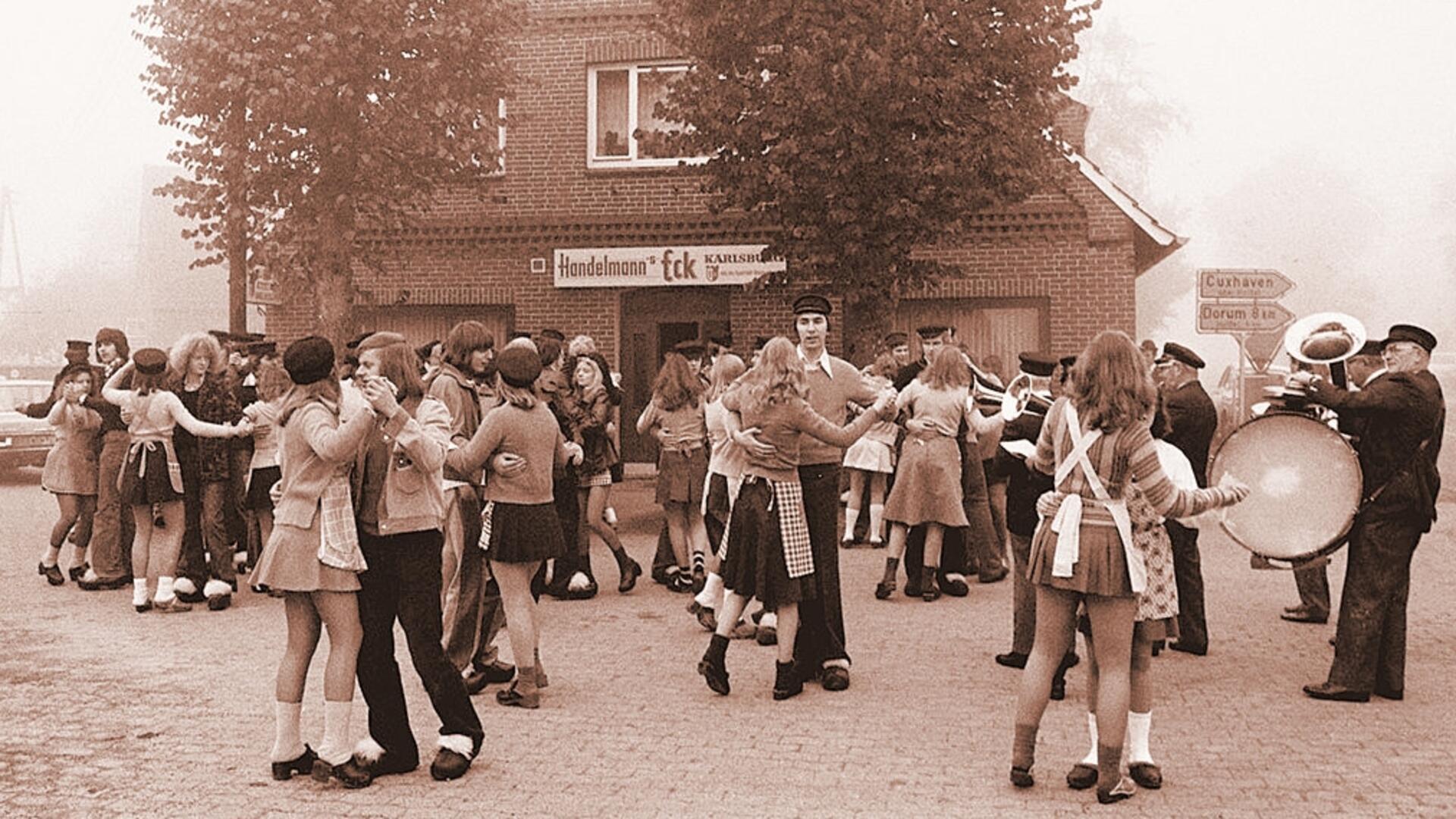 Junge Männer und Frauen tanzen in Holschen auf einem Platz