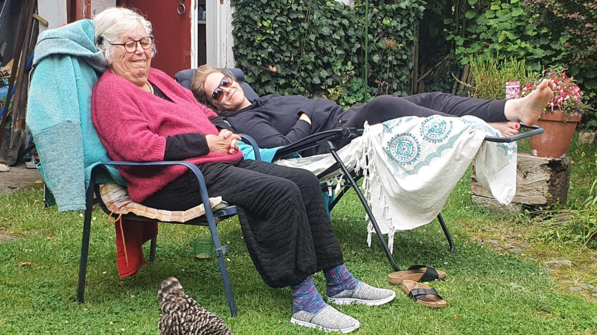 Zwei Frauen in Gartenstühlen davor ein schwarz-weißes Huhn