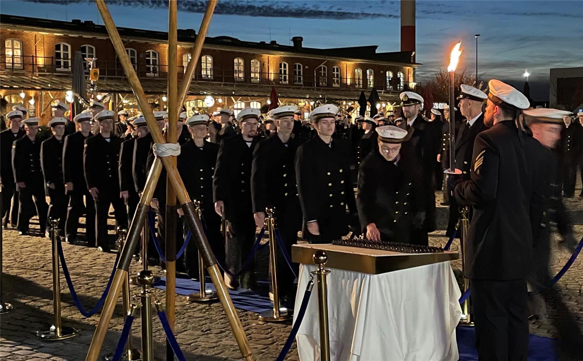 Eine Menschenschlange in schwarzen Uniformen und mit weißen Mützen im maritimen Stil. Die Personen greifen sich Coins.