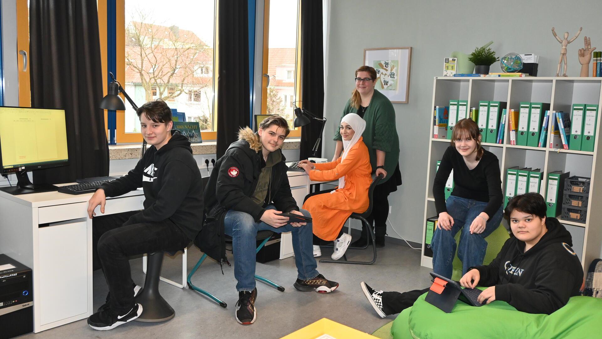 Schüler und eine Lehrerin sitzen in ihrem Redaktionsbüro.