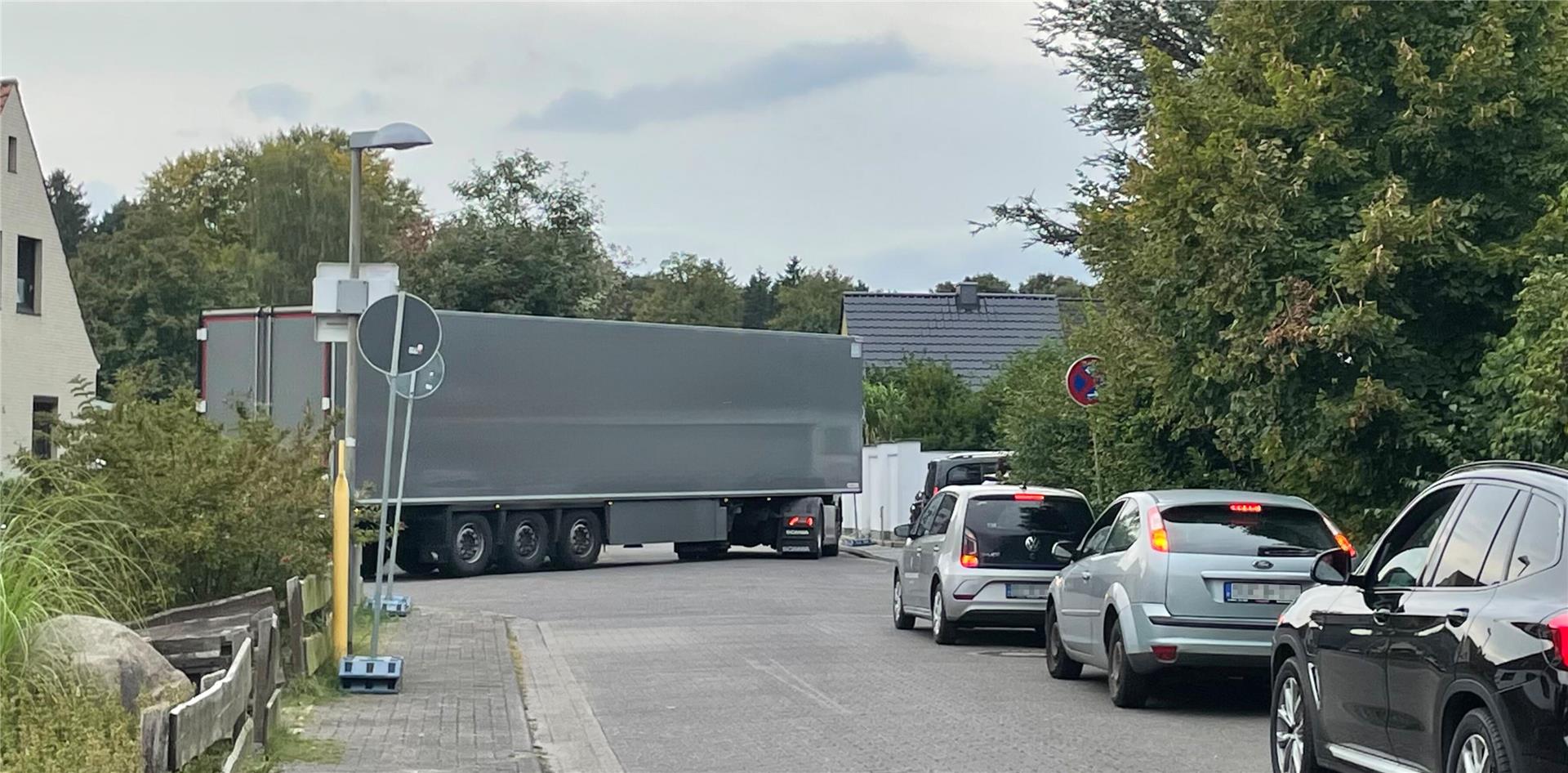 Ein Lkw, der um eine Kurve fahren will. Autos stehen auf der einmündenden Straße und warten.