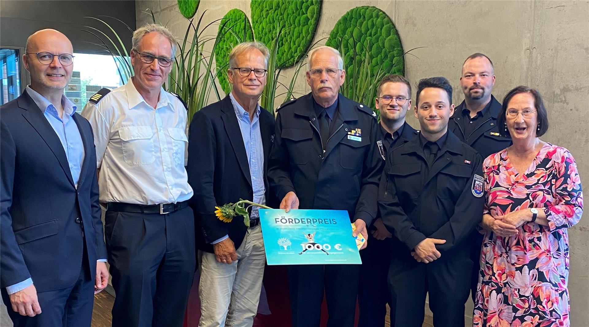 Gruppenfoto bei der Verleihung des Dr. Henning Hübner Förderpreises: Acht Personen stehen nebeneinander, darunter Preisträger Malte Hoheisel in Uniform mit Urkunde und Sonnenblume, umgeben von Mitgliedern der Feuerwehr und der Bürgerstiftung Bremerhaven.