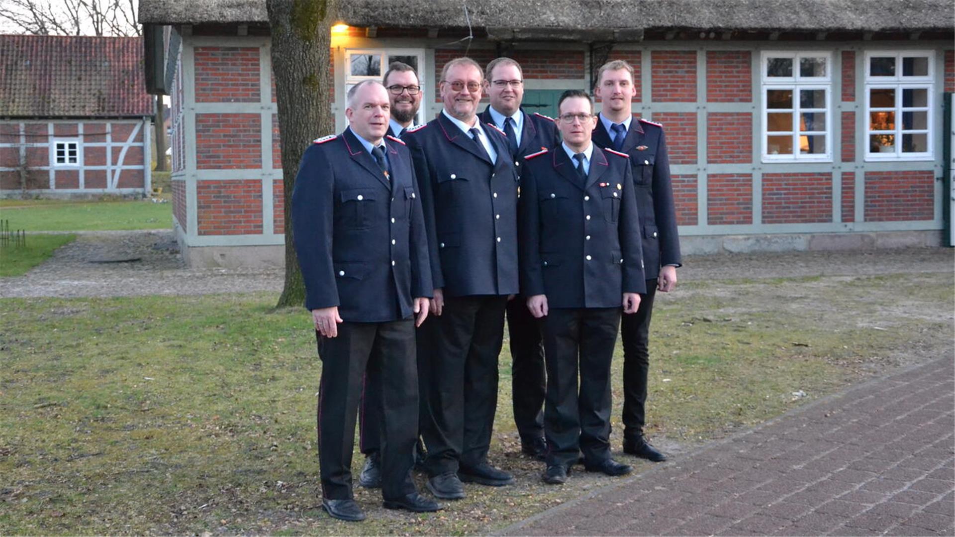 Sechs Feuerwehrleute stehen in festlicher Uniform vor einem norddeutschen Fachwerkhaus.