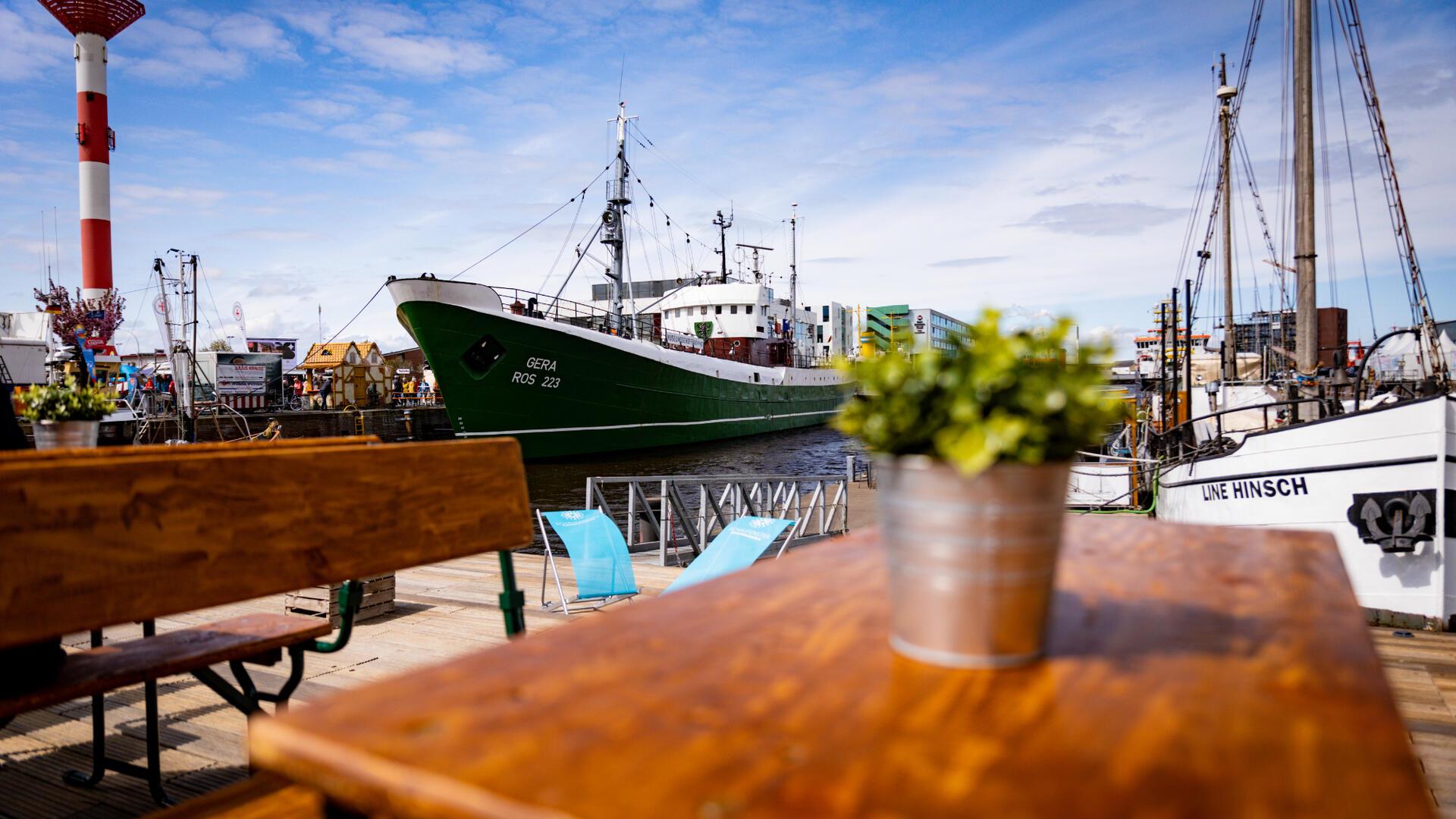 Was kann man in Bremerhaven machen? Tipps für den Besuch in der Stadt am Meer Ein Blick über einen Tisch auf Schiffe, die im Hafen liegen. Die Sonne scheint.