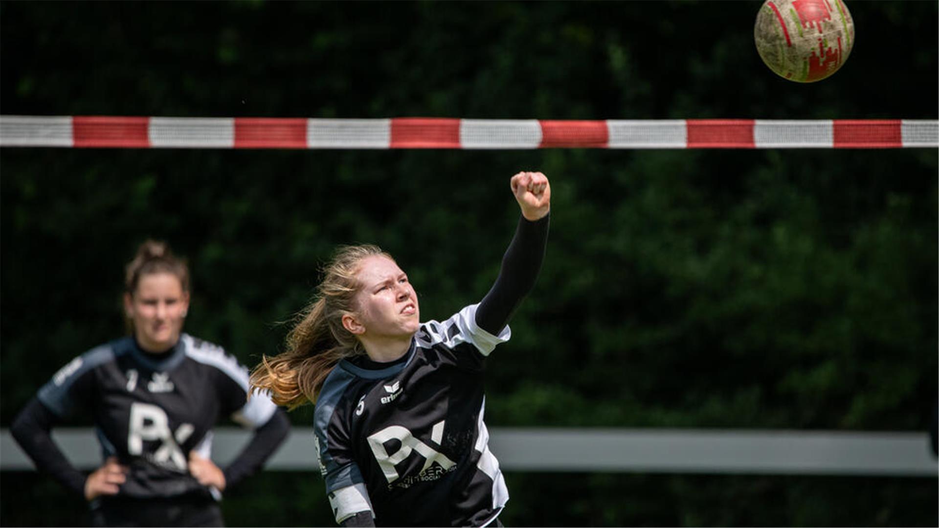 Eine Frau schlägt einen Ball über ein rotweißes Band.