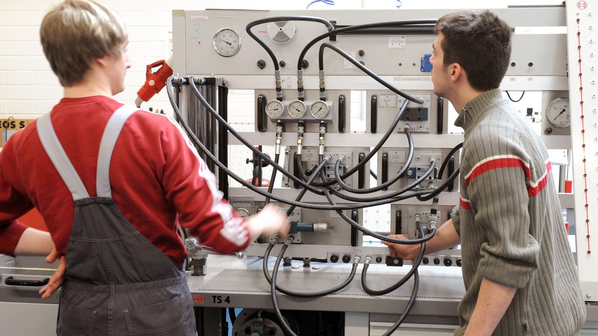 Zwei junge Männer stehen an einer hydraulischen Anlage