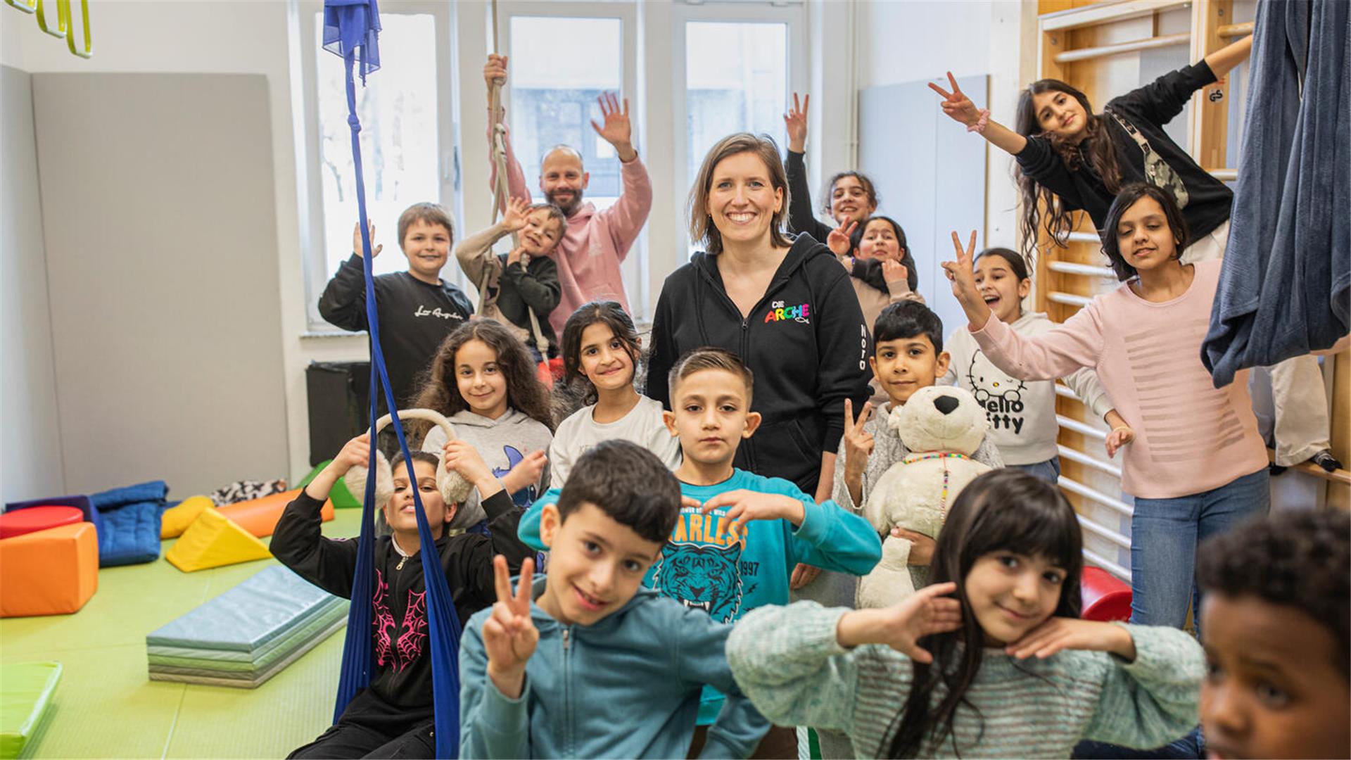 Nora Mengel steht im Mittelpunkt der Arche-Kinder im Bewegungsraum der Einrichtung.