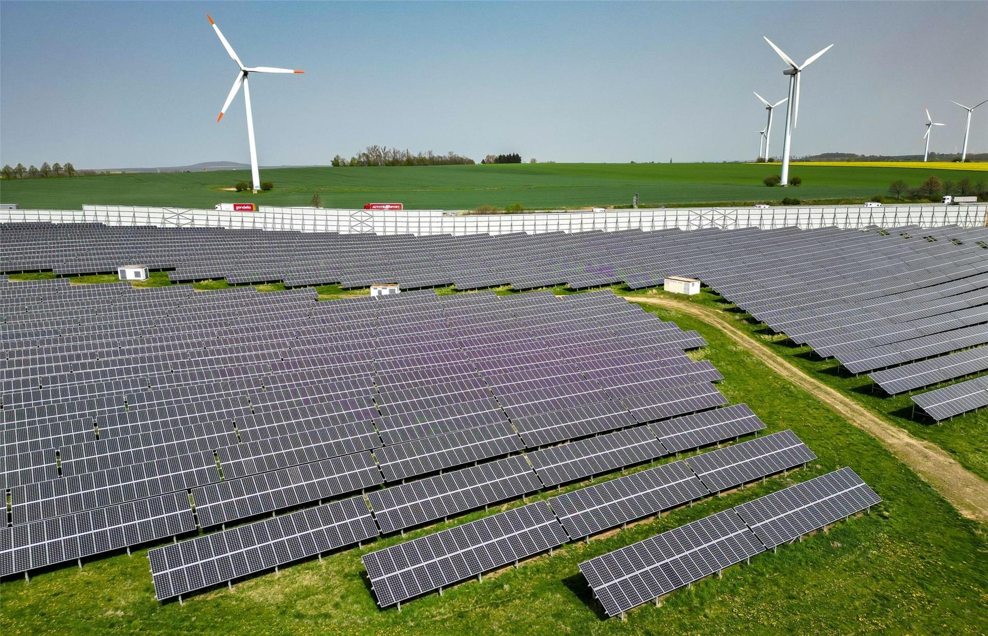 Mehrere Windkraftanlagen stehen hinter einem Solarpark.