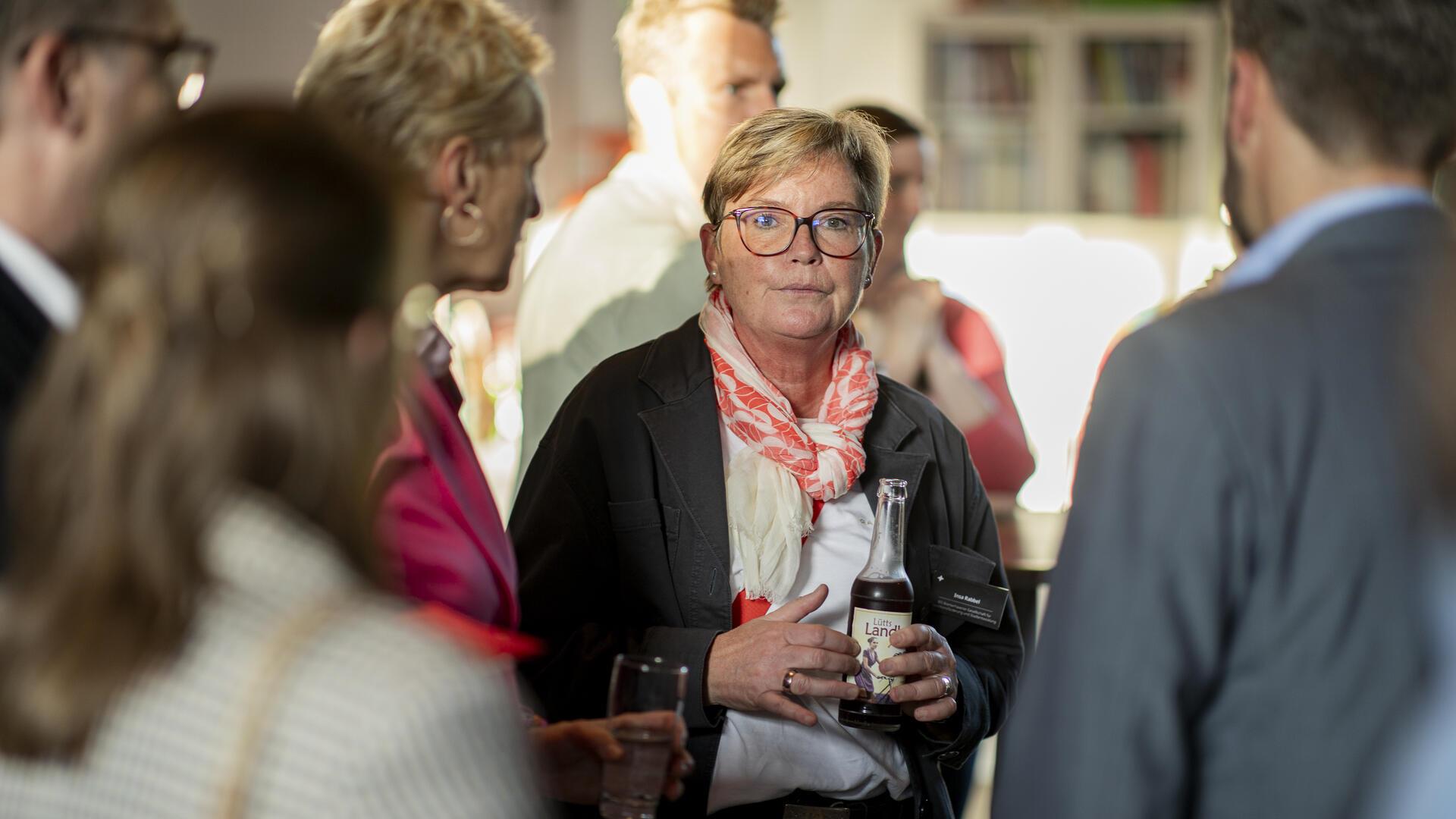 Eine Frau mit Brille, die eine Flasche in der Hand hält.