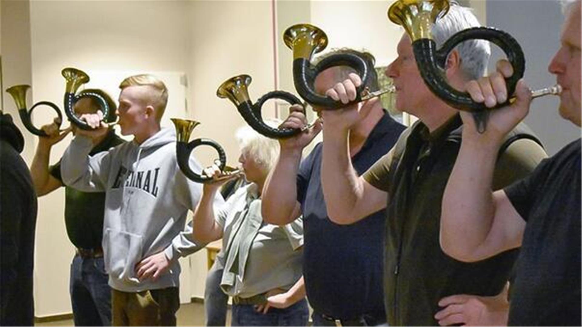 Männer und Frauen blasen in Hörner.