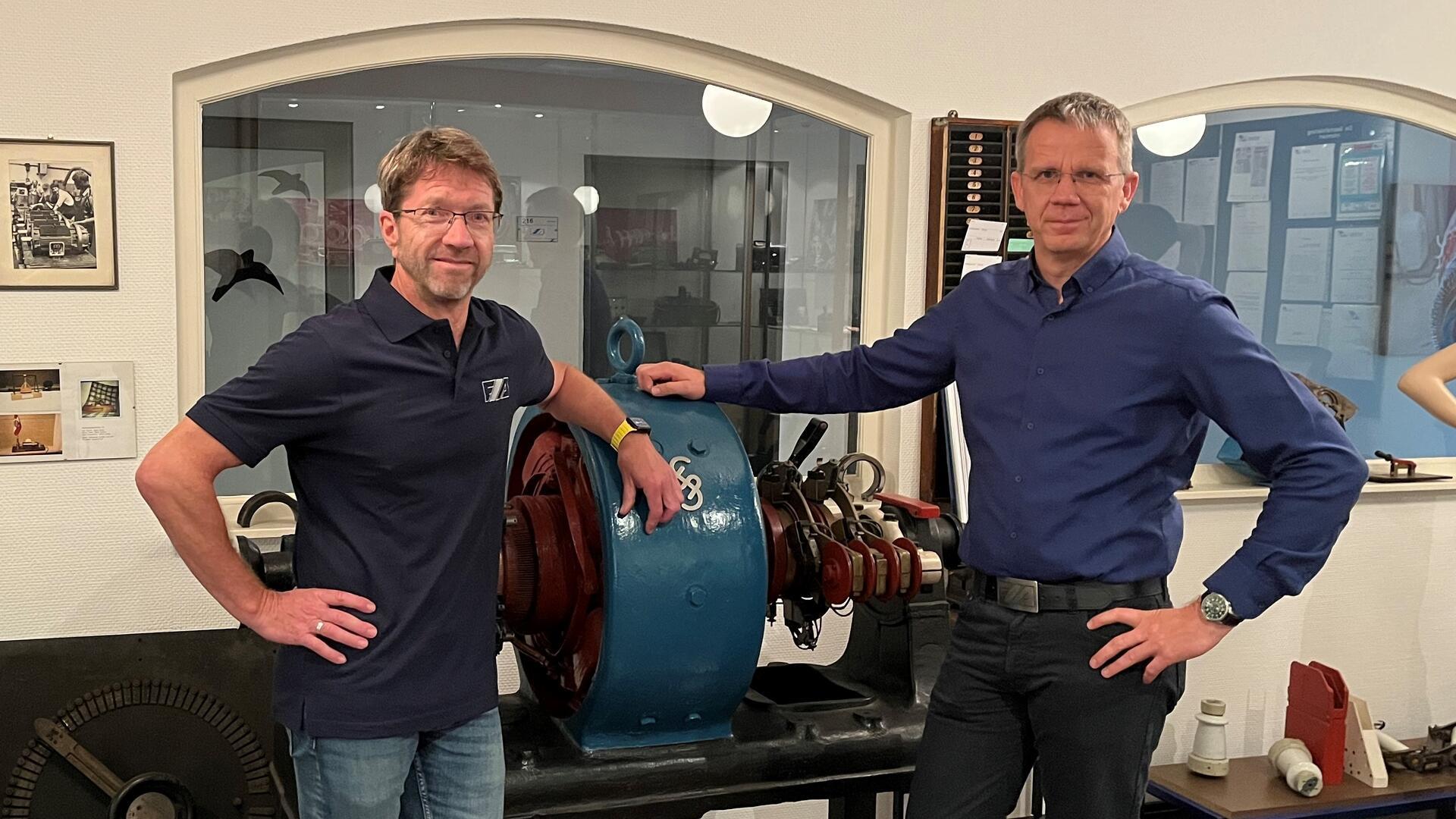 Zwei Männer stehen an einem historischen Motor in einem Museum.