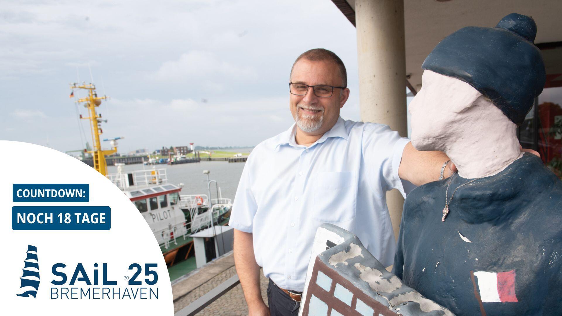 Mann steht neben einer Figur, im Hintergrund ein Schiff