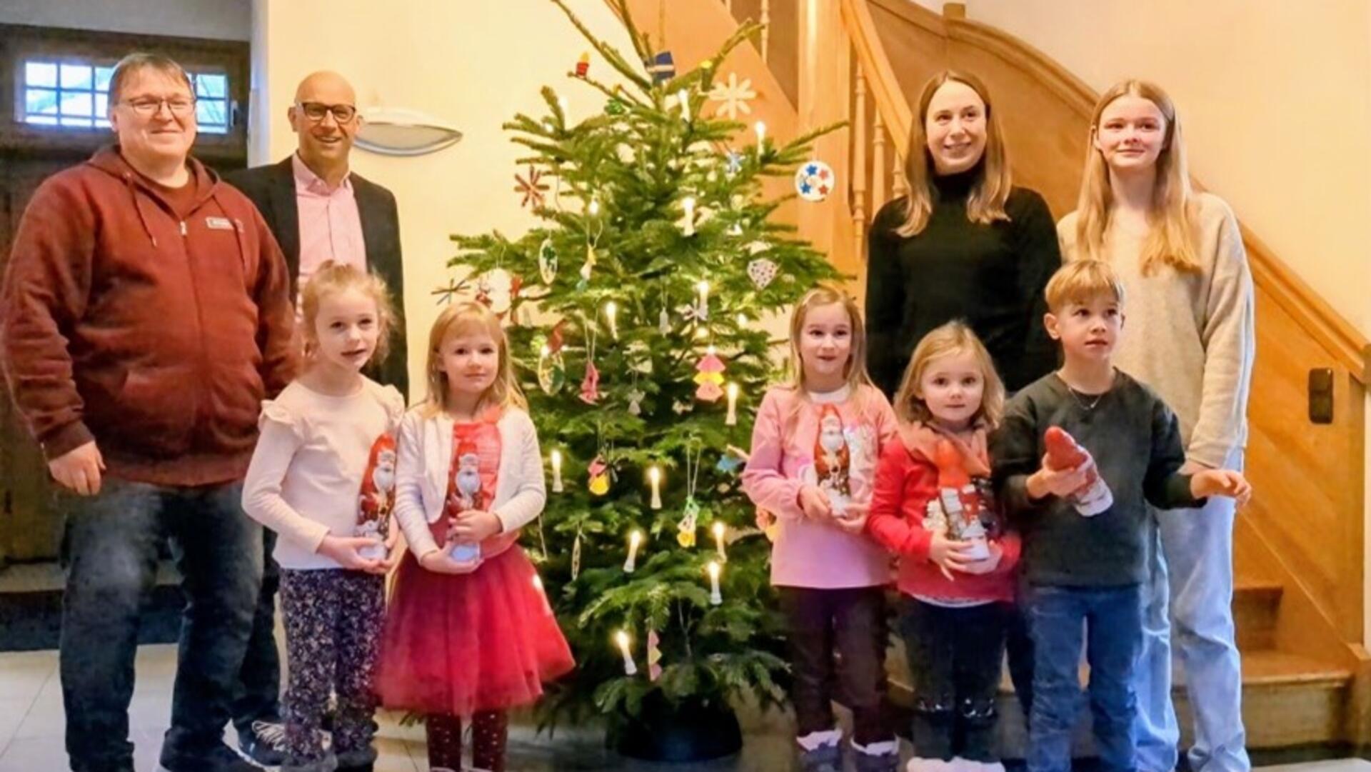 Kinder und Erwachsene stehen vor einem geschmückten Weihnachtsbaum. 