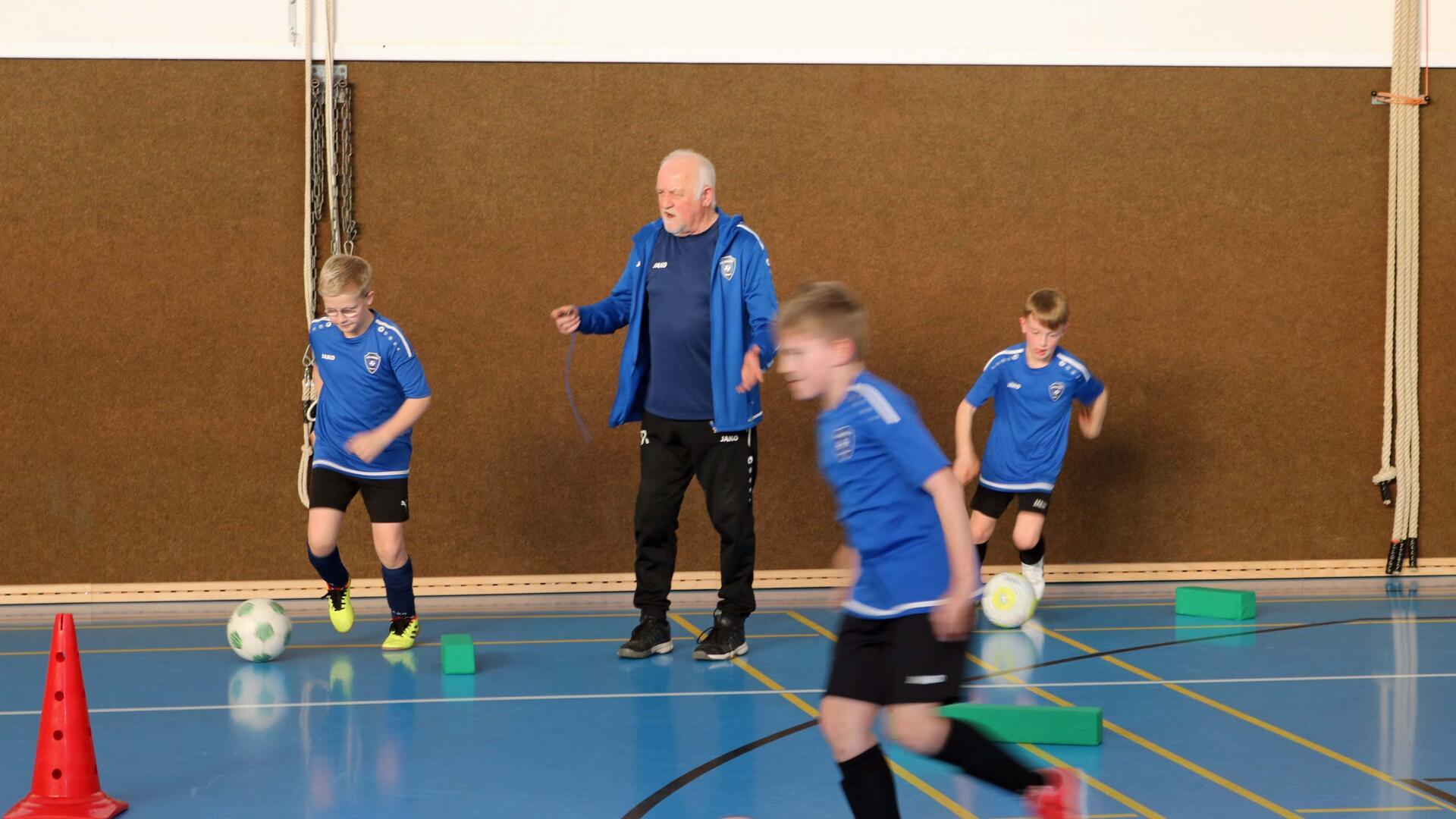 Ein Mann - der Trainer - und drei Jungen in einer Sporthalle.