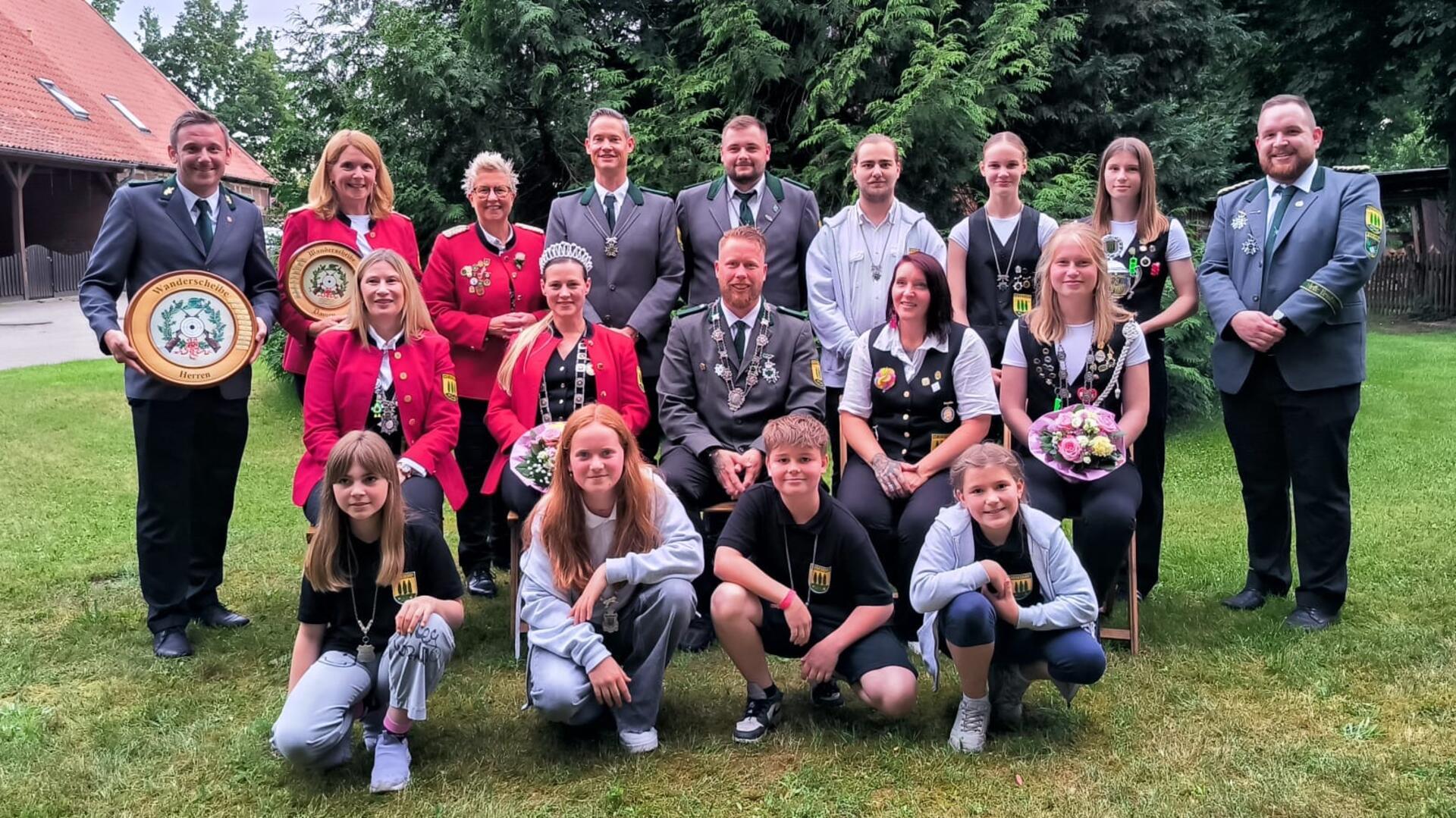 Menschen stehen zu einem Gruppenbild aufgereiht auf einer Grasfläche. 
