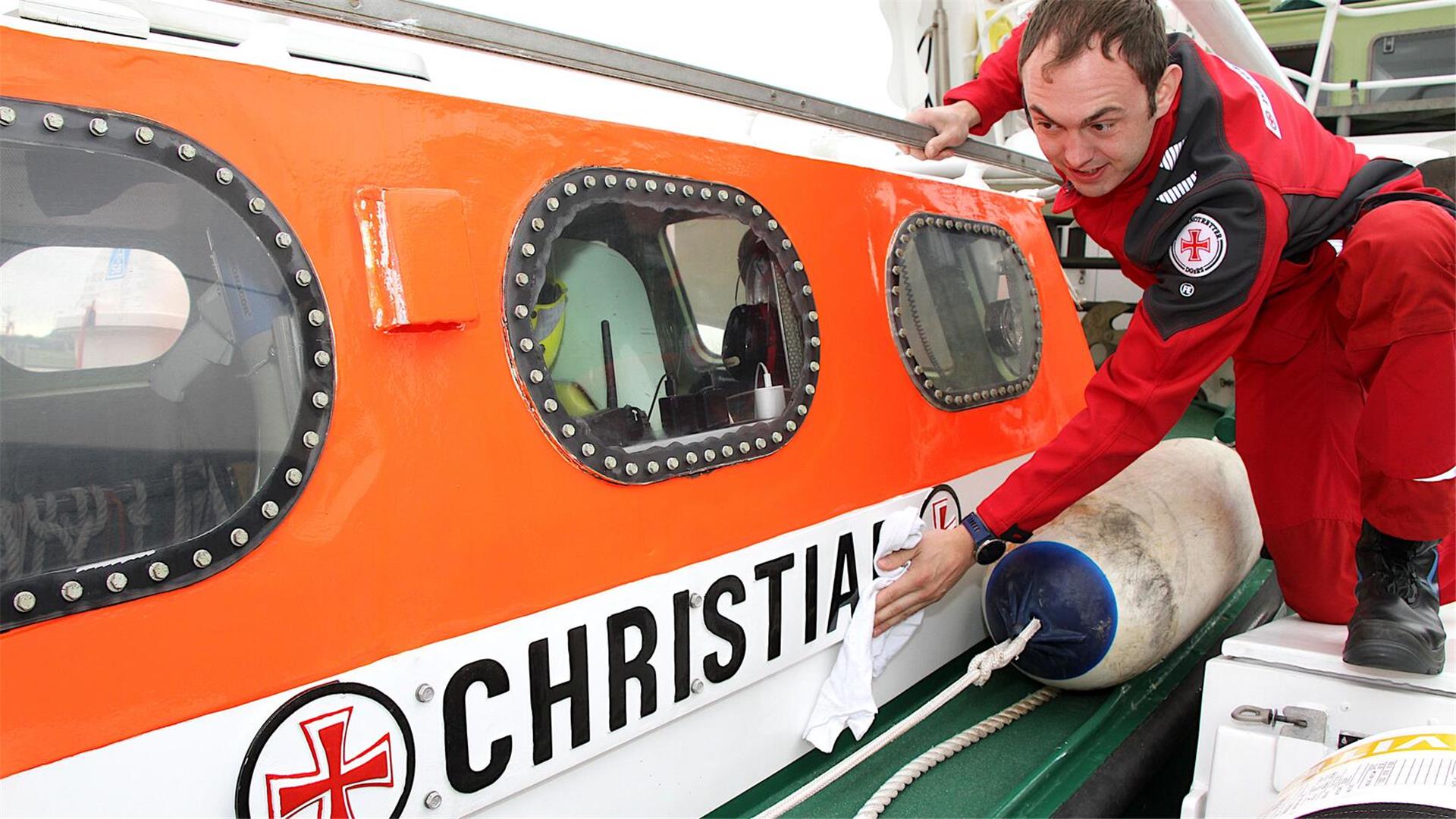 Ein Seenotretter in rotem Overall poliert das Tochterboot „Christian“ der „Hermann Rudolf Meyer“ an dessen orangem Rumpf