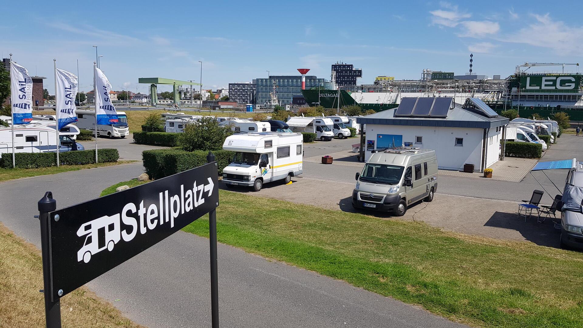 Ein Schild mit der Aufschrift "Stellplatz" steht vor einem Stellplatz für Wohnmobile. 