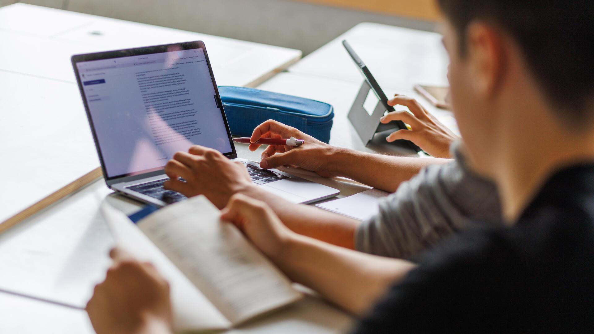  Schüler sitzen vor einem Computer und benutzen ein KI-Tool. 