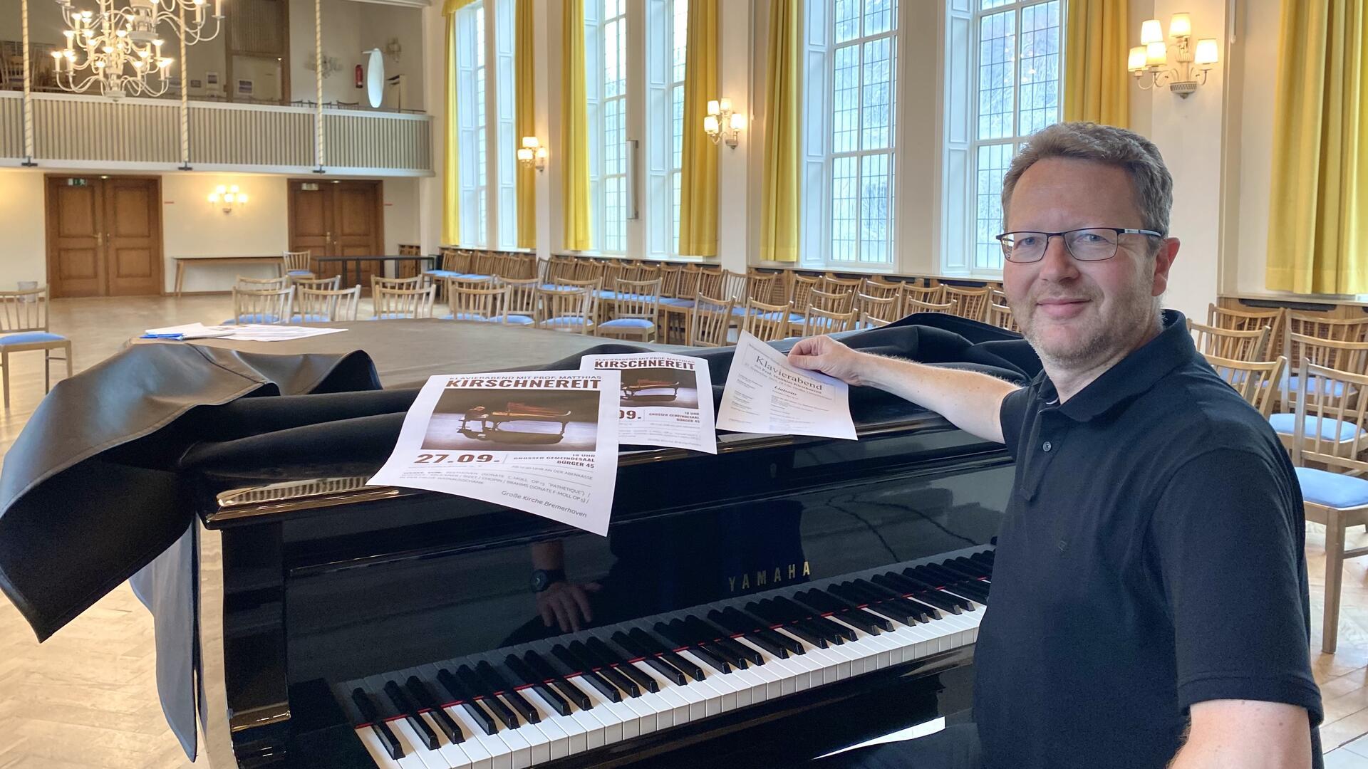 Ein Mann sitzt an einem Klavier und schaut in die Kamera. Landeskirchenmusikdirektor und Kantor David Schollmeyer in Bremerhaven ist glücklich, den renommierten Pianisten Matthias Kirschnereit für einen großen Solo-Klavierabend  im Saal der Großen Kirche Bremerhaven gewonnen zu haben.