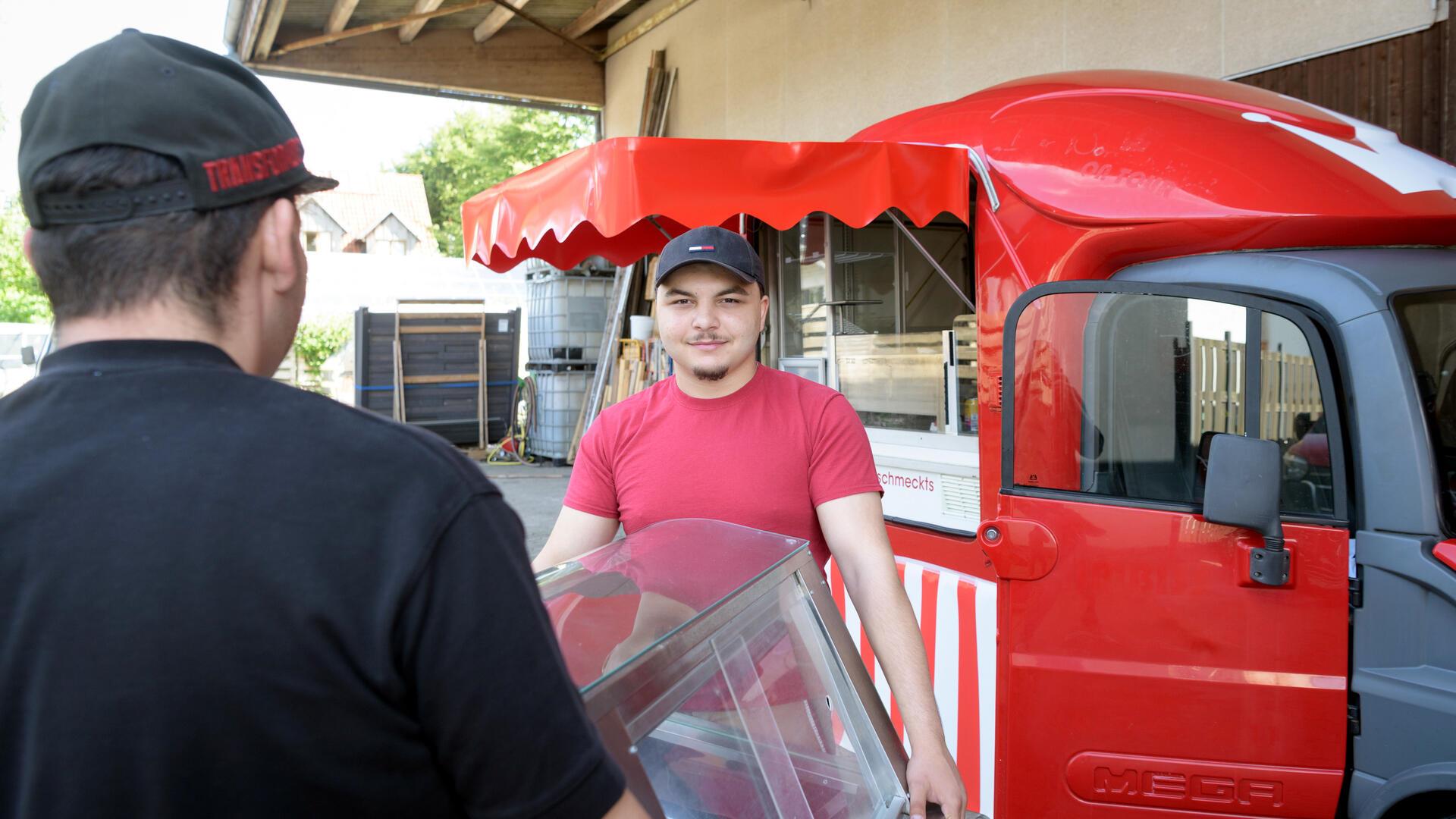 Zwei Männer tragen eine Kühlvitrine zu einem roten Foodtruck