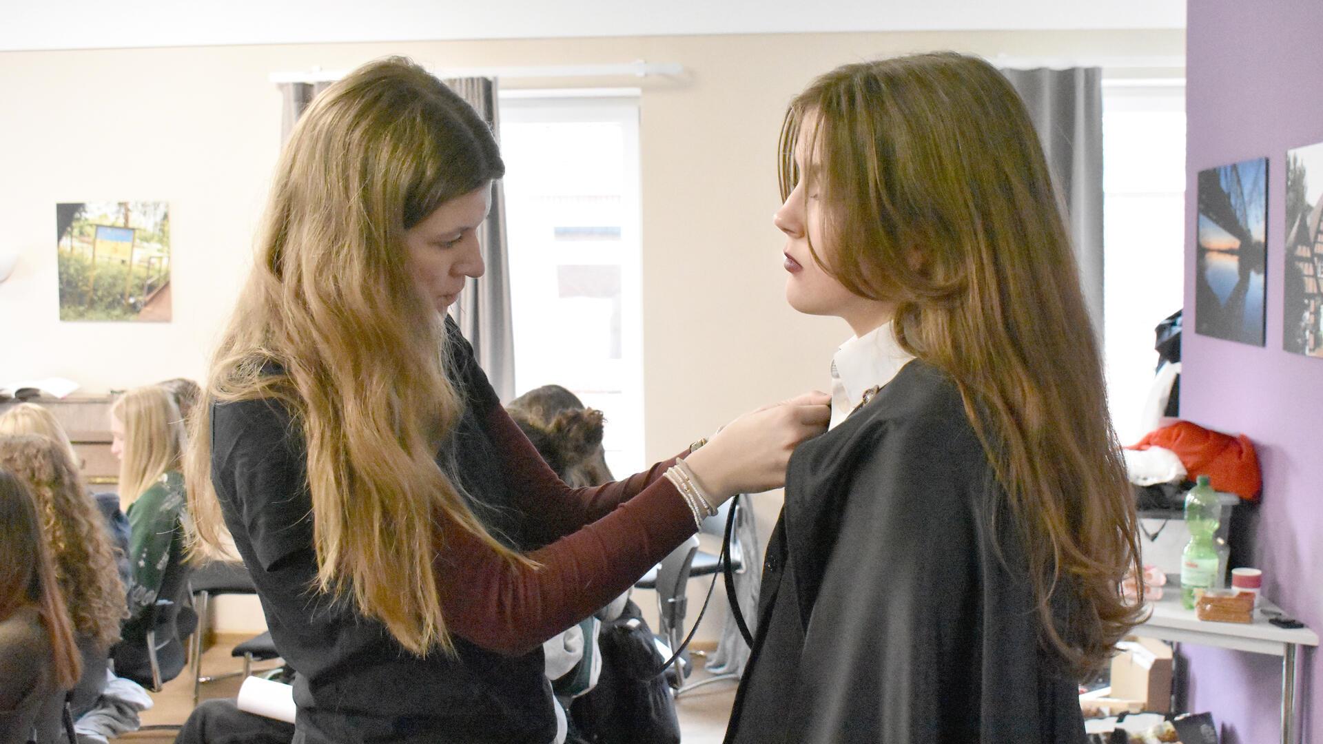 Zwei Mädchen mit langen Haaren stehen nebeneinander und befestigen etwas an einem Kragen.